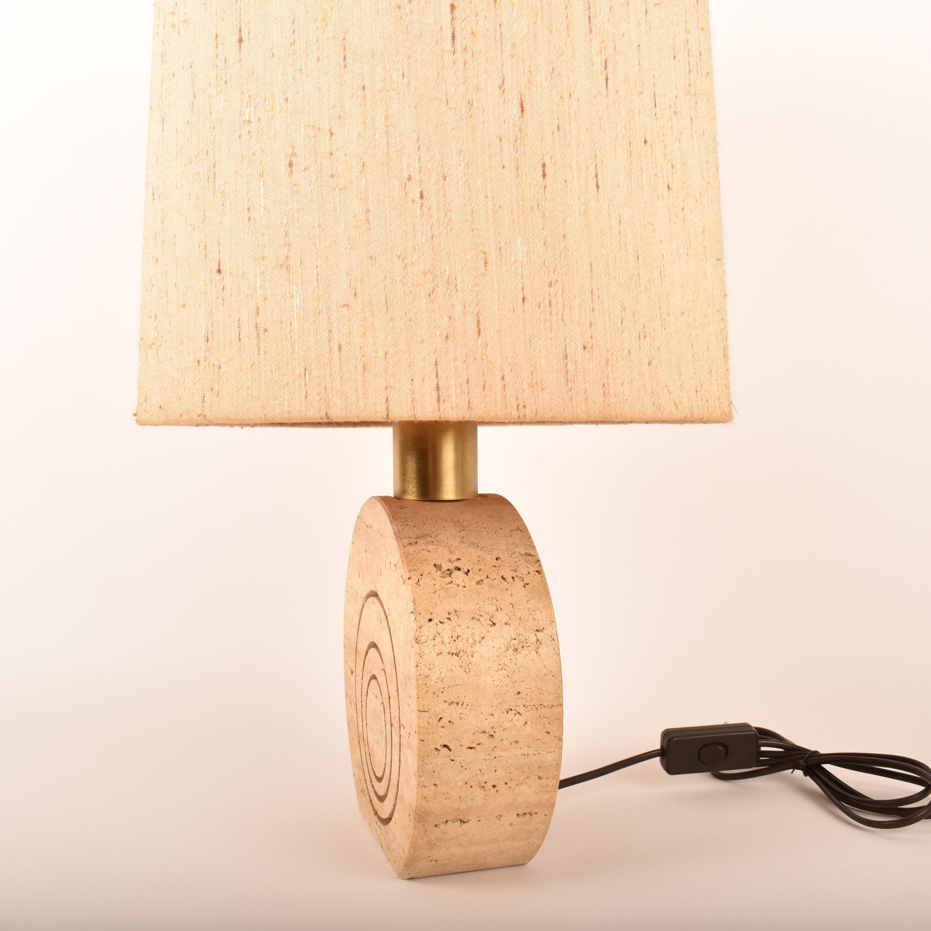 Lampe de table iconique, conçue et fabriquée par Fratelli Manelli en Italie vers 1970.
La lampe est en travertin, avec des gravures de cercles concentriques, de couleur crème. 
L'abat-jour est en très bon état, toujours d'origine, et donne une belle