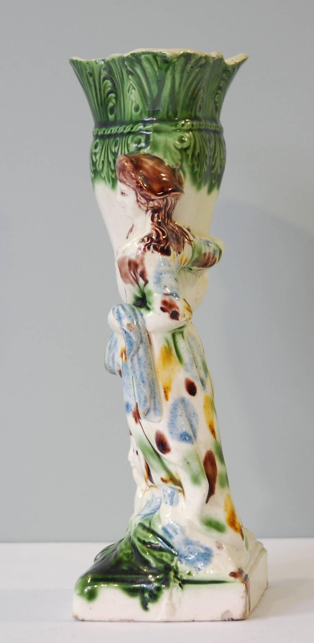 In creamware, decorated with colors under the glaze (Prattware); depicting a young lady standing by a decorative vase and a fountain. This example dates from the time English potters were just starting to gain control of colored glazes.

A rare