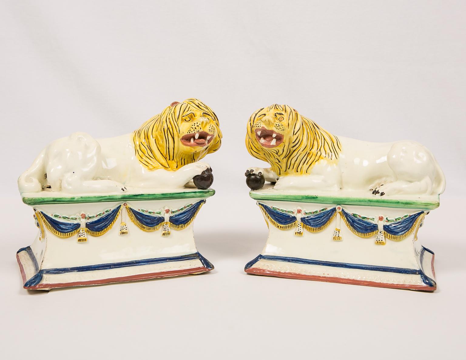 We are thrilled to offer this exceptional pair of creamware lions, each elegantly resting on a tall base adorned with sumptuous swags of dark blue 