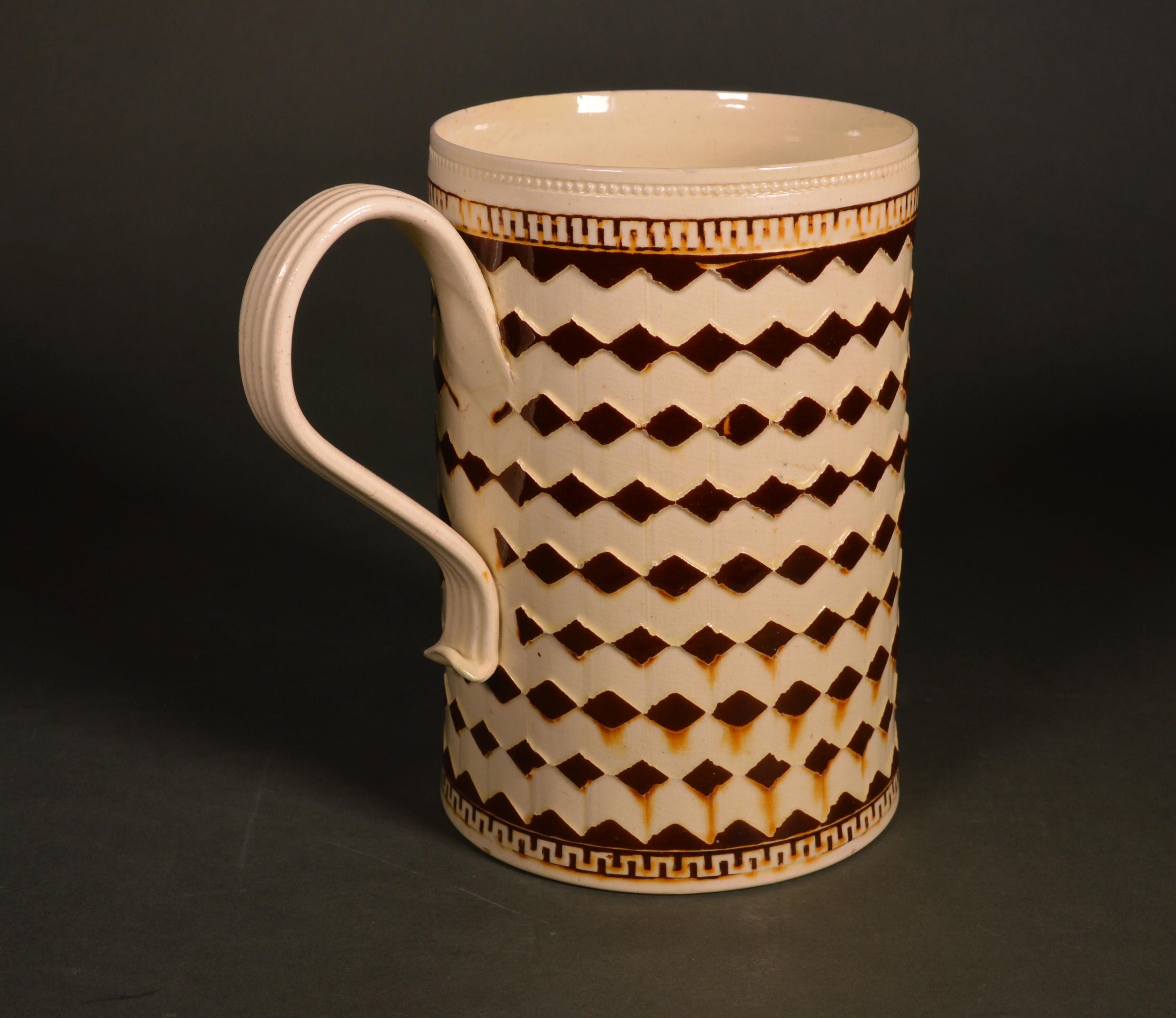 Stunning creamware mocha large tankard with bands of diamonds,
circa 1800-1820,
  

The charming and striking cylindrical mug with a creamware body is decorated with nine bands of raised diamonds colored brown. At the foot and rim is a Greek key