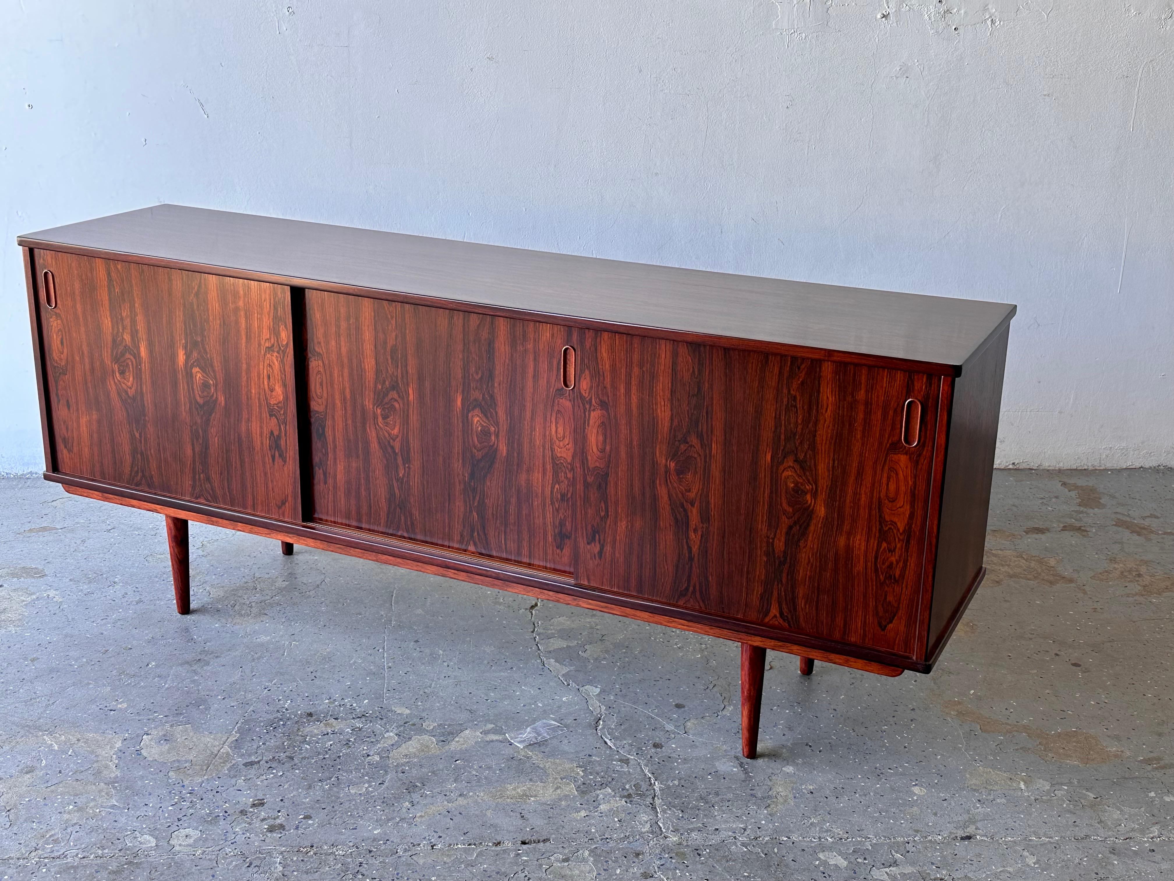 Danish Modern Dyrlund rosewood Credenza / Sideboard 

Made in Denmark by Dyrlund 
Features Three (3) Sliding Doors, with One (1) Shelf in the Left and Two (2) Shelves in the Center Section

Two (2) Slide-Out Flatware / Napkin Drawers on the Right