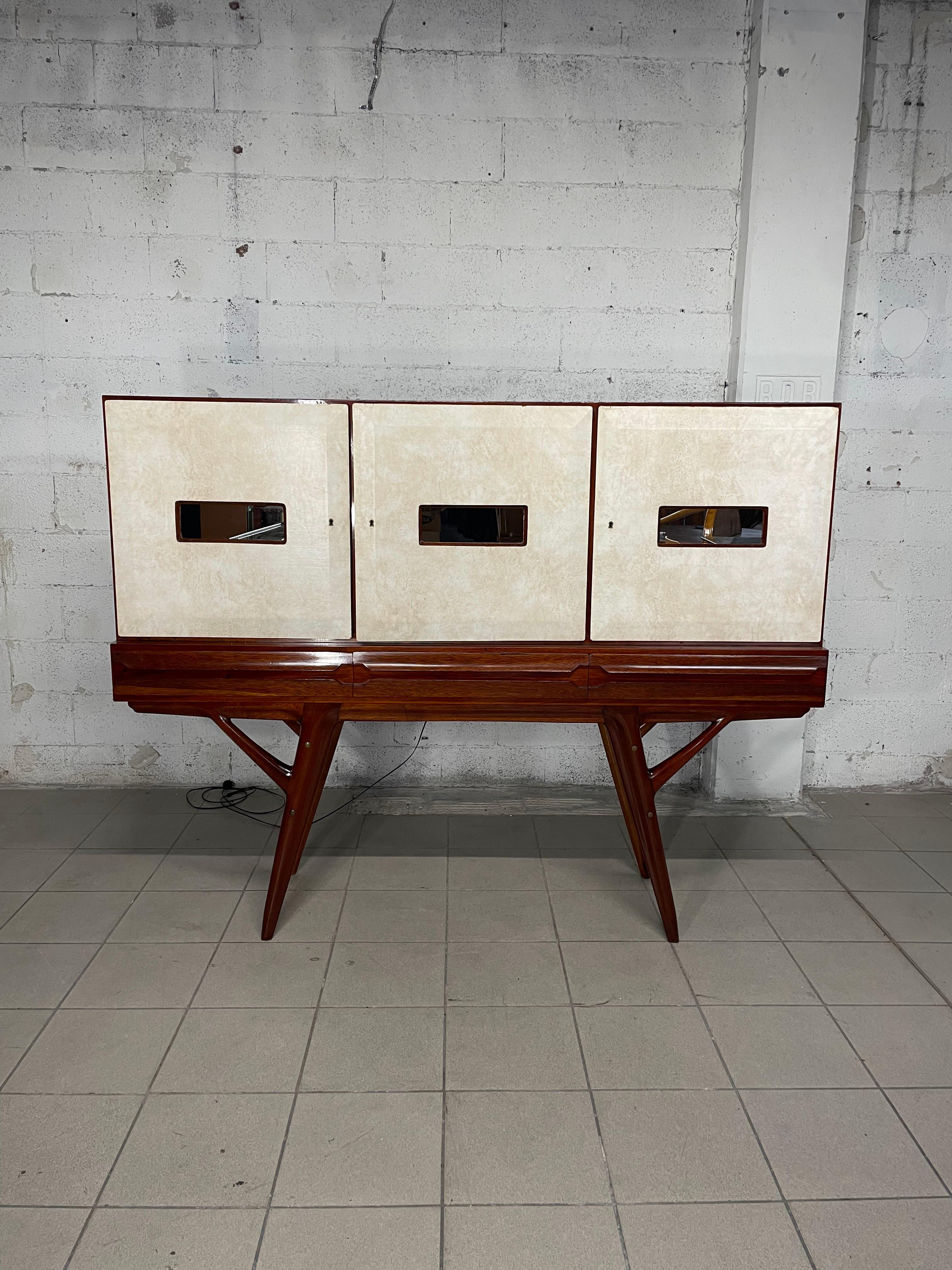 1950s sideboard with mahogany wood frame and parchment-covered doors with central panes of mirrored glass.

In addition to the 3 doors, there are 3 drawers at the base and mirrored interiors that can transform the sideboard into a bar cabinet.

The