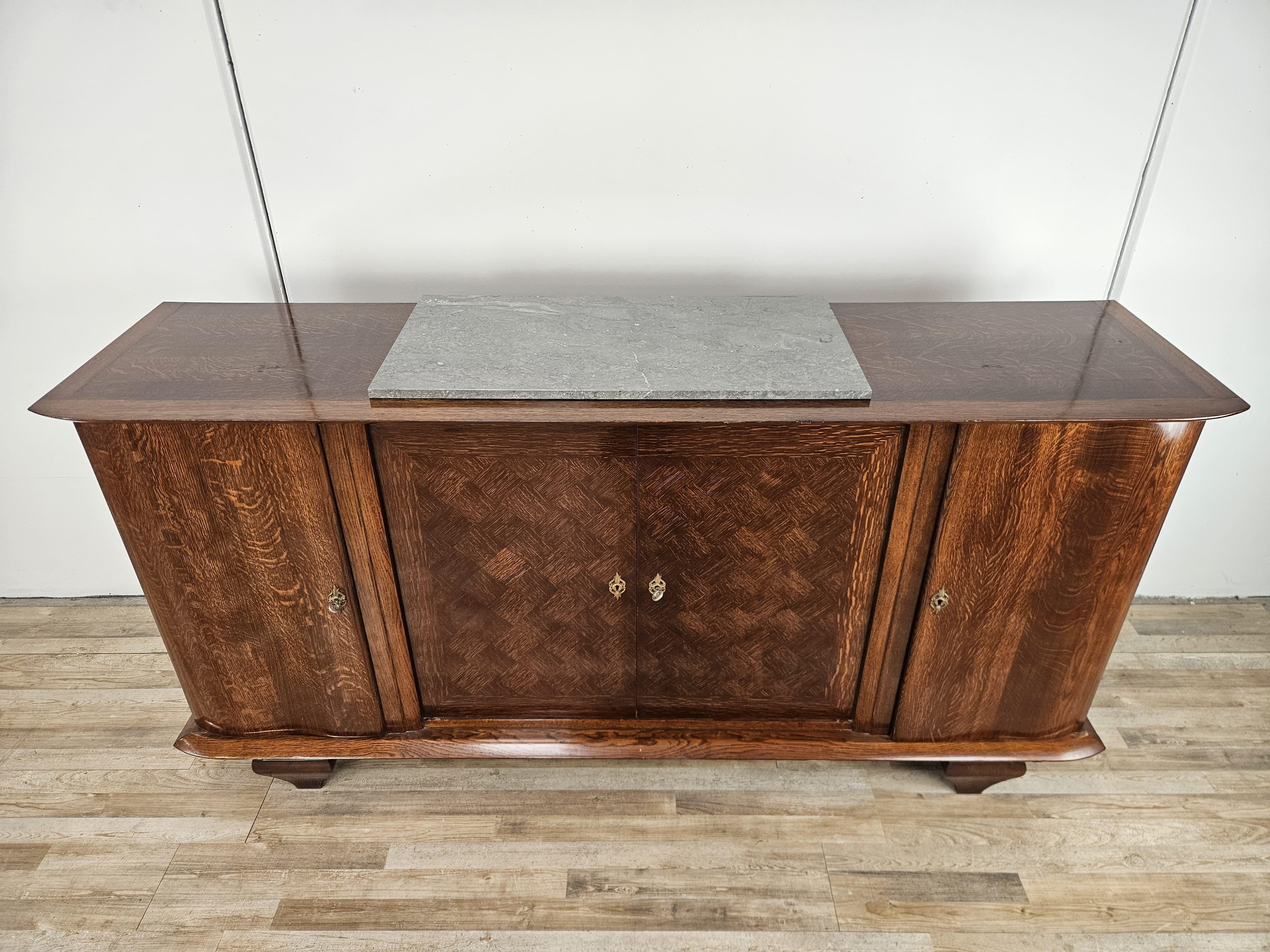 Credenza Art Decò anni '50 in rovere con un particolare gioco di forme a scacchiera sul piano principale.

Il cellulare si presenta con due ante laterali dotate di ripiani interni e un piccolo cassetto, al centro si trova uno scomparto con