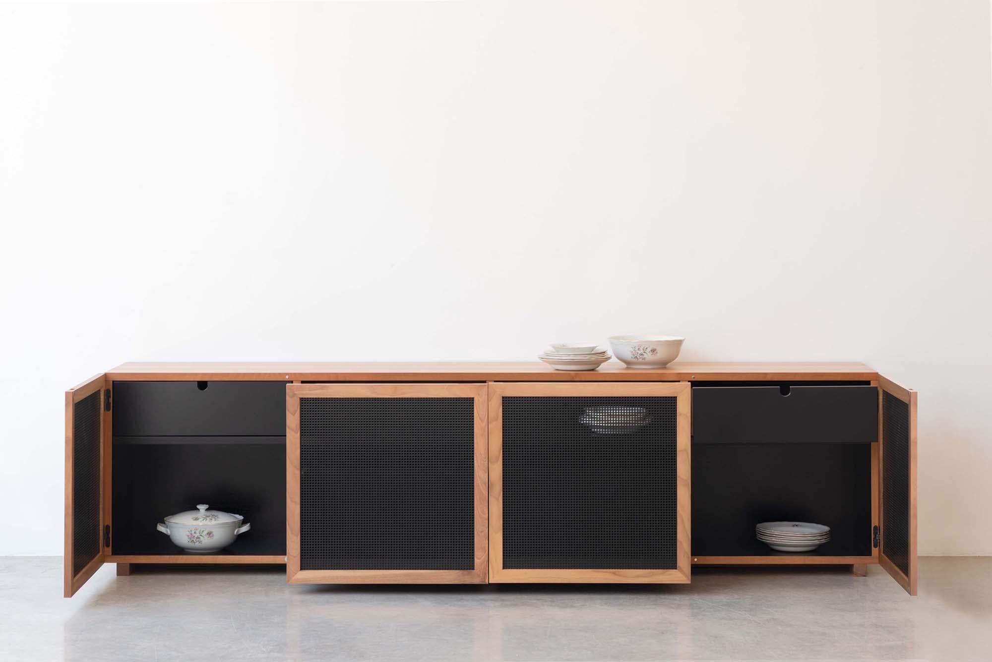 A rectangle with clean, extremely linear shapes, which expresses an essential refinement: the low sideboard is a container in walnut wood, which hides dark, lacquered shelves and drawers.
On the front, the perforated sheet metal doors give air and