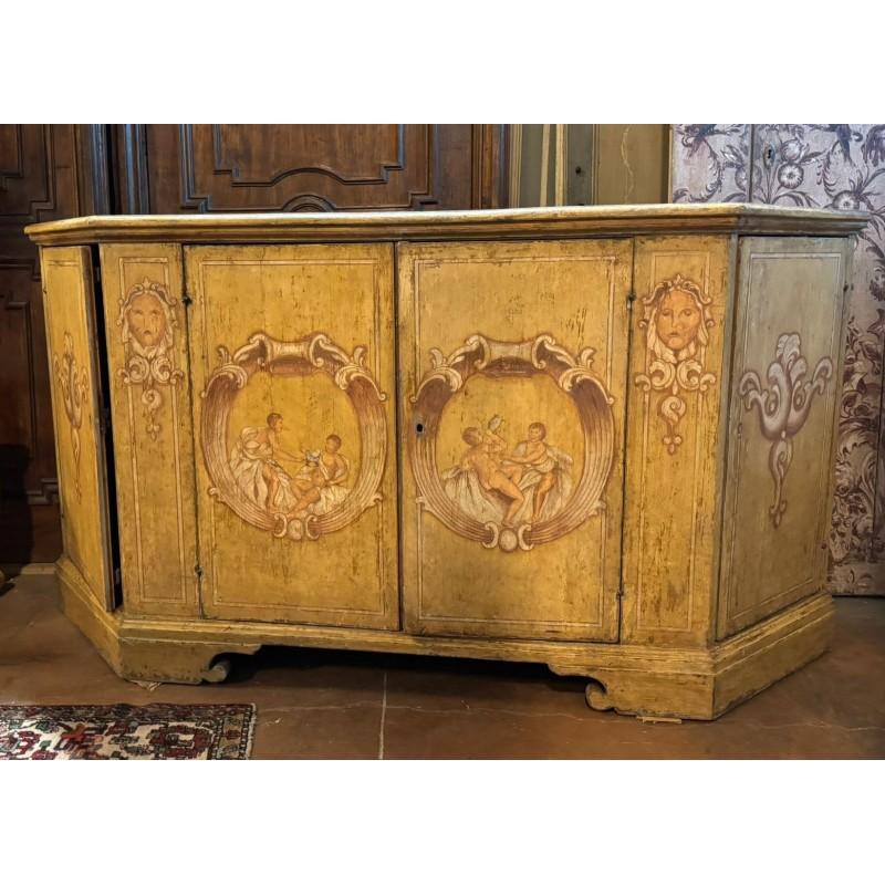 Antica Credenza, stipo basso in legno laccato e riccamente dipinto con figures, di putti e decori baroccheggianti. Fondo giallo con figure rosso terra, Presenta quattro ante (2 sono i laterali apribili) con ripiani interni. Originale di Epoca '700,