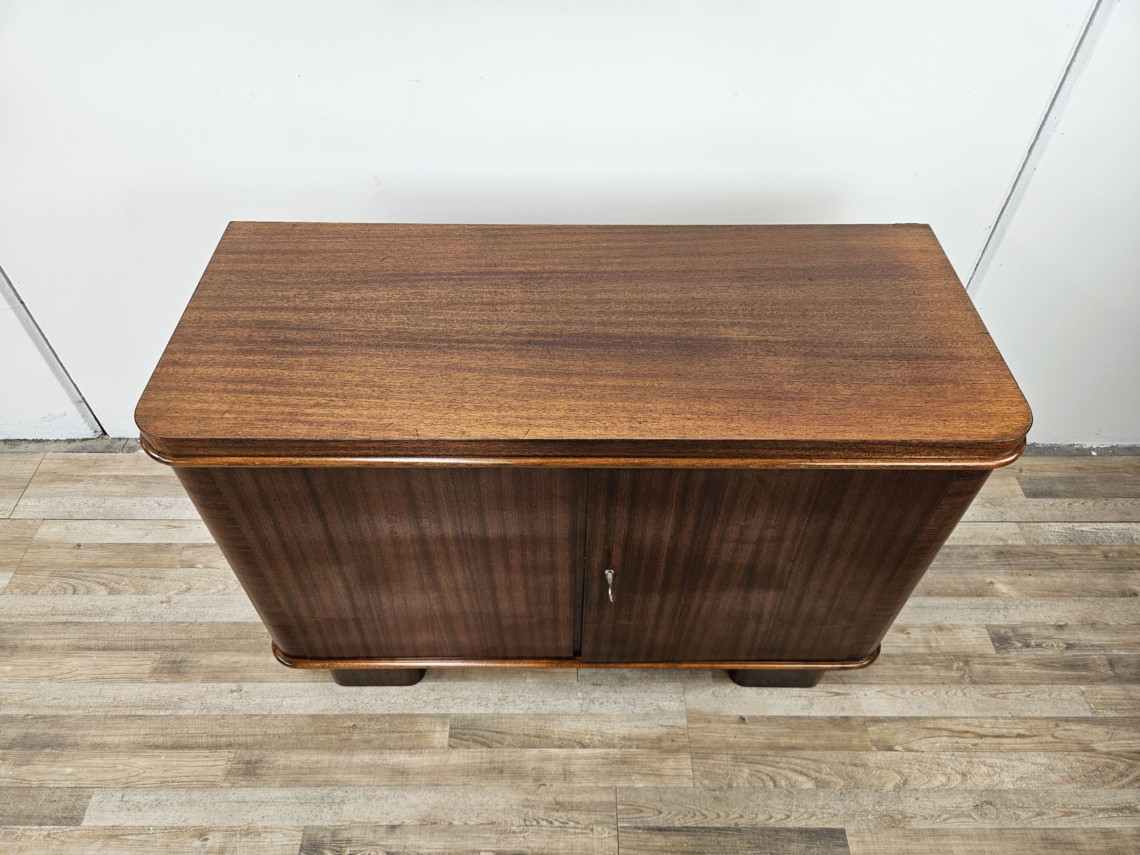 Piccola credenza dei primi anni '50 di origine tedesca, realizzata in piuma di noce con ripiani e un doppio cassetto interno.

Si presenta con delle misure lineari e contenute, perfettamente adattabile ad ogni tipologia di locale o arredo grazie al