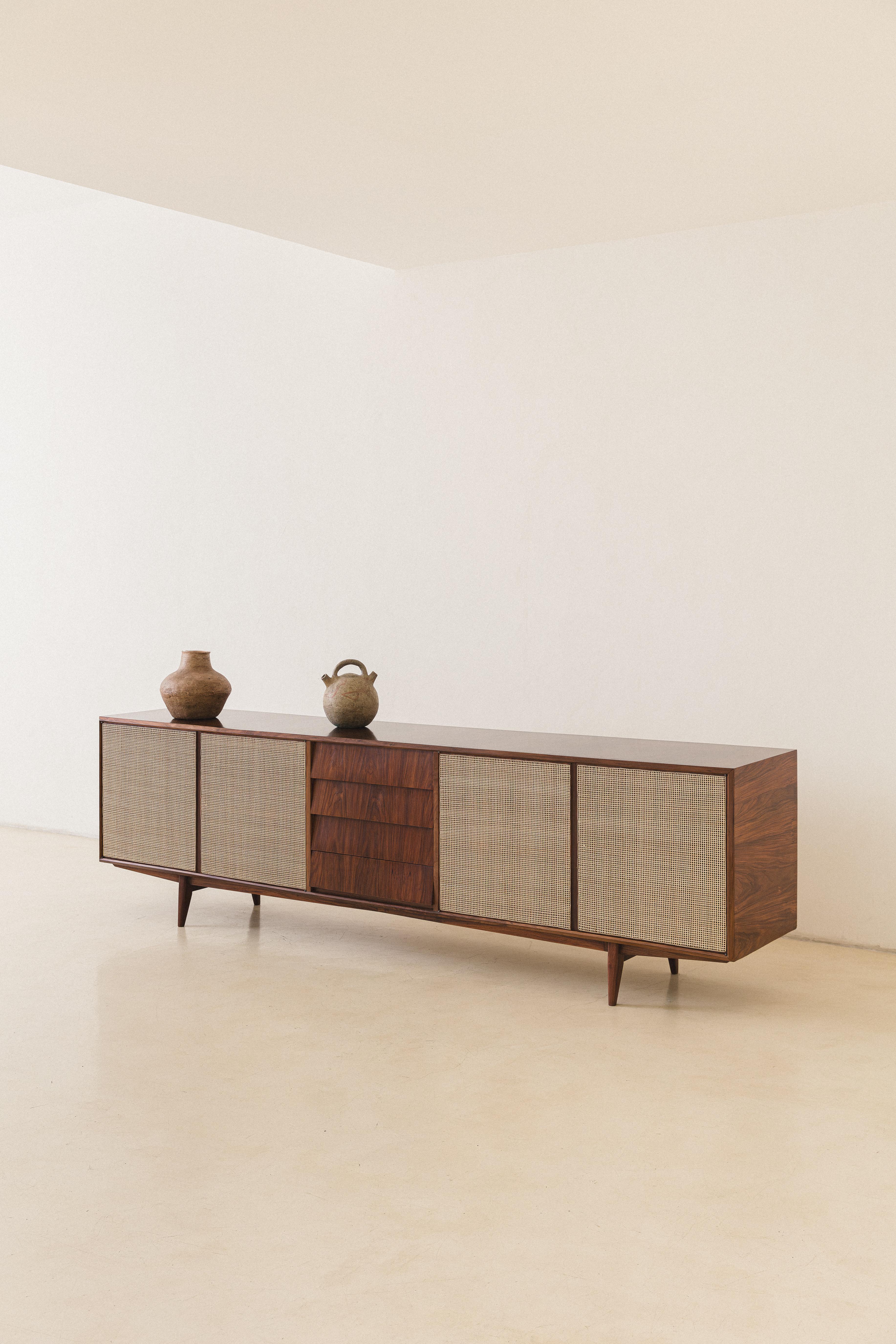 This Credenza was produced by the Brazilian company Tapeçaria Schulz S.A in the 1950s, capturing the eye. 

Made of solid Caviuna and cane, it has four-door compartments and four carefully made drawers. The item showcases distinctive construction