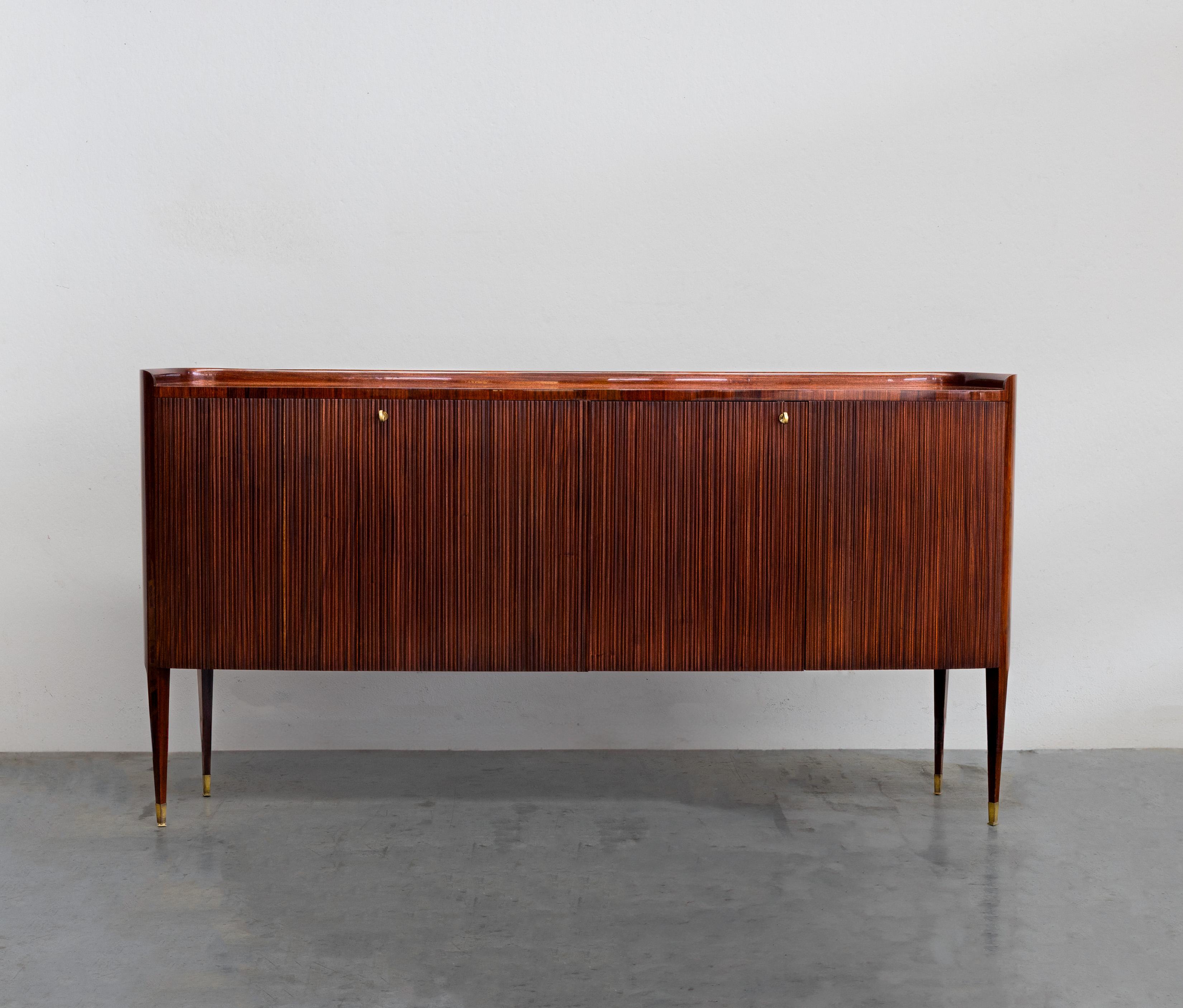 Credenza resting on 4 high legs by Paolo Buffa, A Riva Mobili d’Arte Milano.
The piece of furniture has two “compartments”, each closed by double hinged doors.
The left part is fitted with 2 shelves, the upper element on the right serves as a bottle