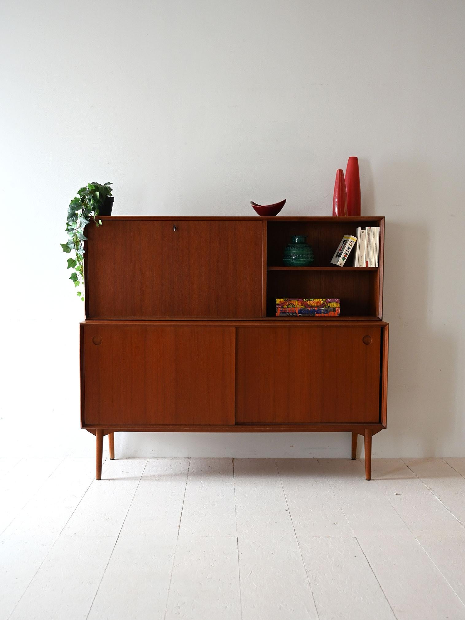 1950s/60s teak sideboard with flap door, sliding doors and original mark still present.

Example of Danish 1950s/60s manufacture, with teak frame and light proportions. The lower section features two sliding doors with recessed handles, while the