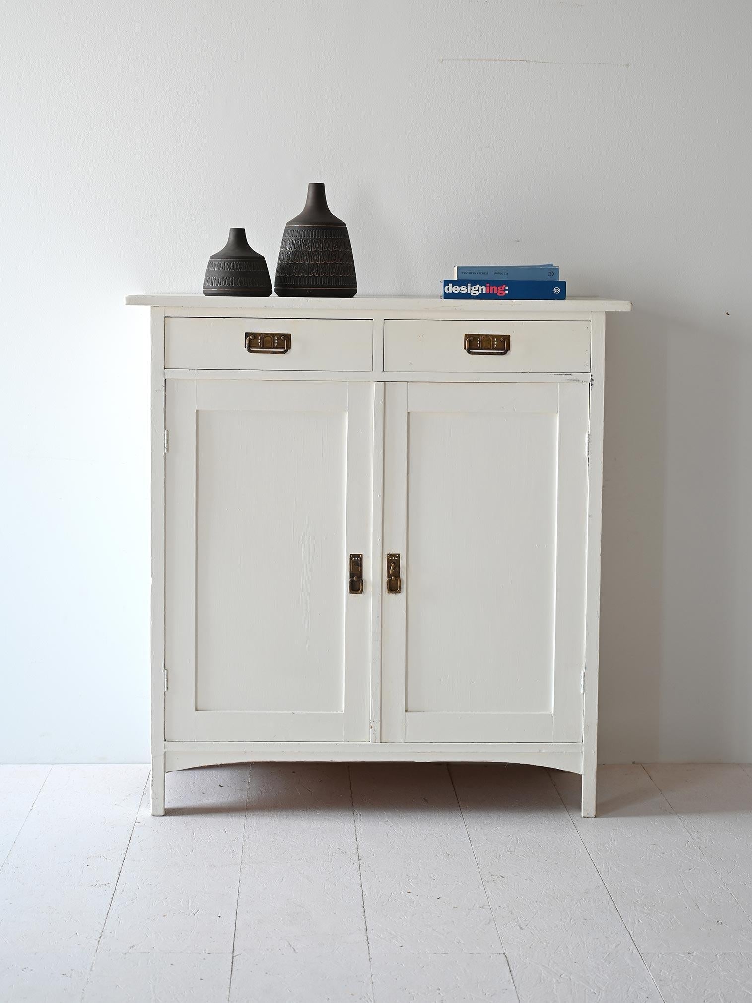 Original Scandinavian vinatage sideboard with two hinged doors and two drawers.

White-painted wood and gold metal handles give the cabinet an elegant look with retro charm. Inside, the space is divided by wooden shelves. 
Good conditions. Potrebbe