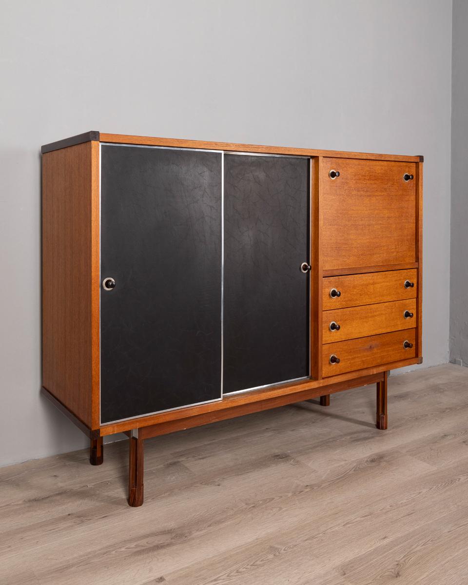 Teak wood sideboard with two sliding doors upholstered in black leather, with drawers and flap. Design George Coslin for 3V Furniture, 1960s.

CONDITION:
In good condition, may show signs of wear given by time.

SIZING:
Height 108 cm; Width 139.5