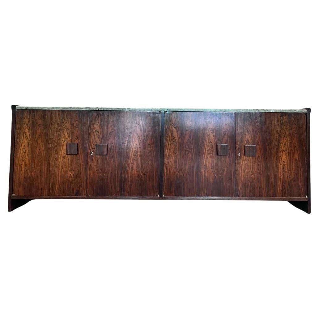 Disponibile da oggi, questa credenza unica nel suo genere è realizzata in palissandro brasiliano e presenta quattro ante, 2 cassetti con maniglie scolpite, 7 vani portaoggetti e un meraviglioso piano in marmo. Il legno è stato magistralmente