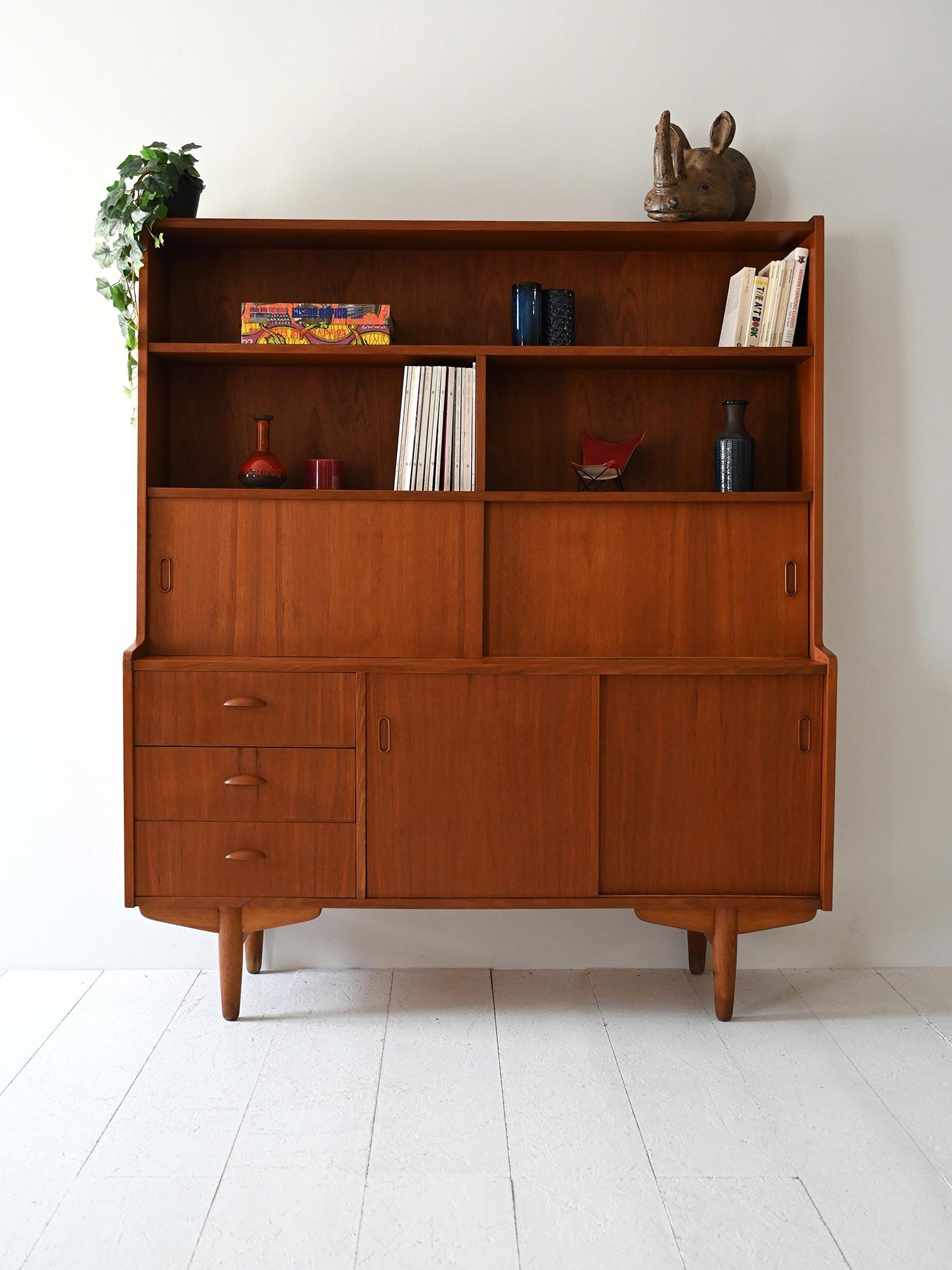 Mobile alto in teak con libreria integrata, cassetti e ante scorrevoli. Design funzionale con linee morbide e compatte.

Credenza scandinava vintage realizzata in teak, databile tra gli anni ’50 e ’60. La parte superiore ospita una libreria a