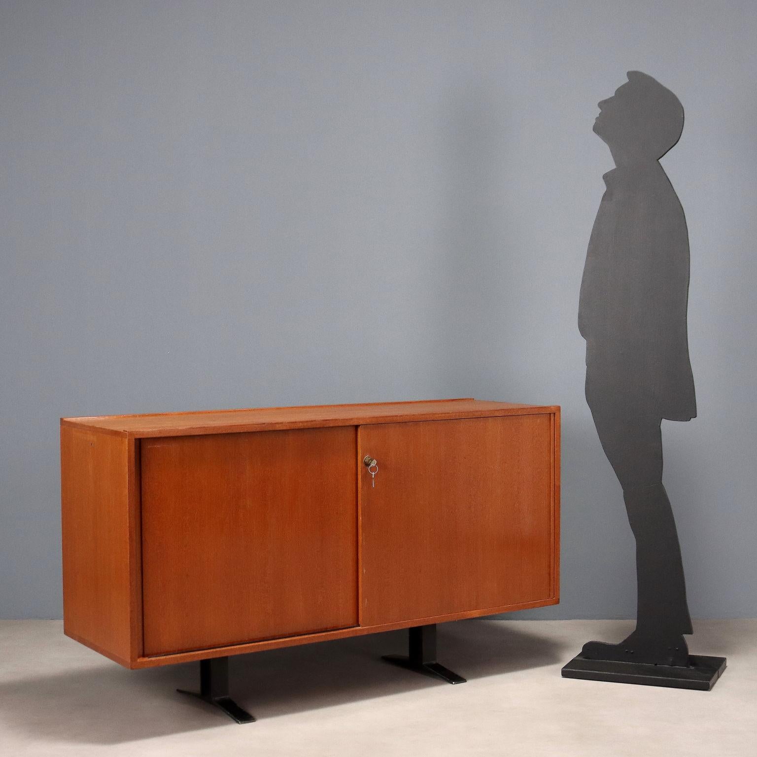 Aparador con puertas correderas de madera chapada en teca y patas de metal esmaltado. Mueble en buen estado general con signos del paso del tiempo, faltan baldas interiores. 