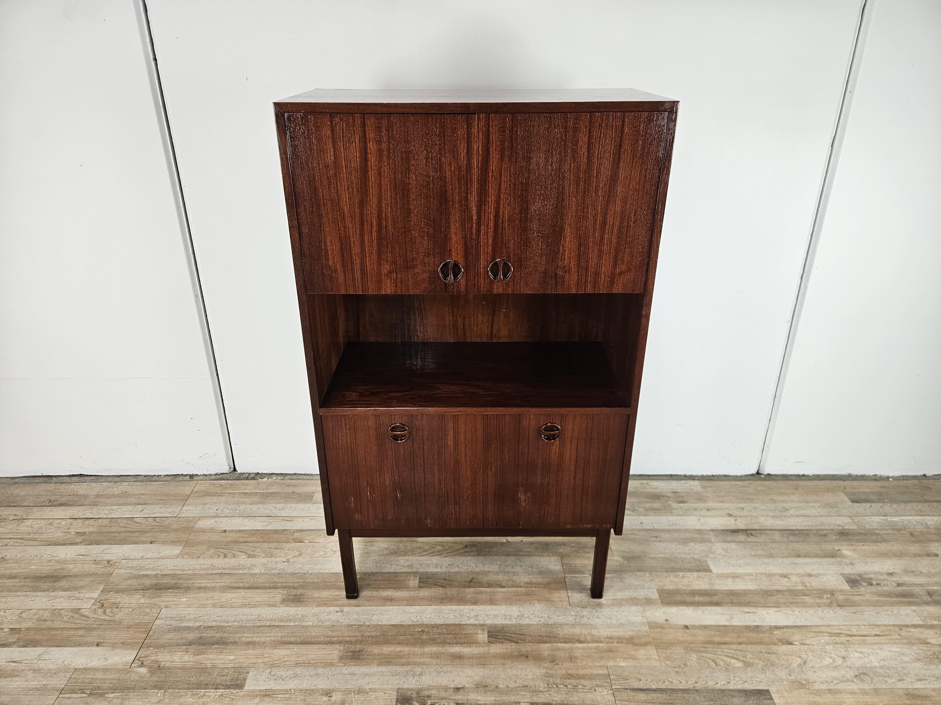 Piccola credenza da soggiorno o studio in teak anni '60.

Presenta un doppio sportello nella parte superiore con ripiani interni e una ribalta alla base.

Molto fine ed elegante, collocabile ovunque grazie alle misure contenute e alle proporzioni