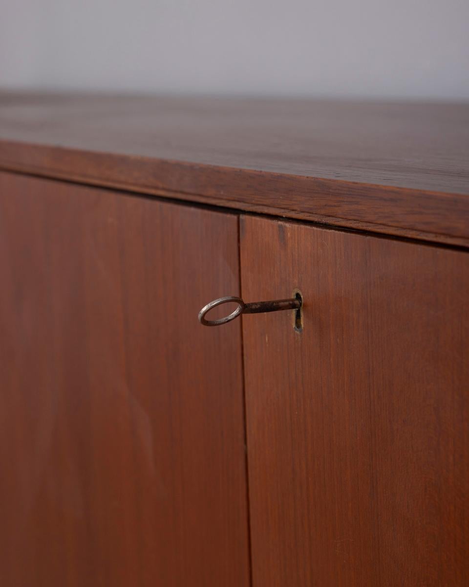 Credenza in legno di teak con cassetti centrali, un'anta a ribalta a sinistra e due ante a battente a destra, entrambe con serratura, design italiano, anni '60.

CONDIZIONE:
En buen estado, presenta signos de uso debidos al paso del