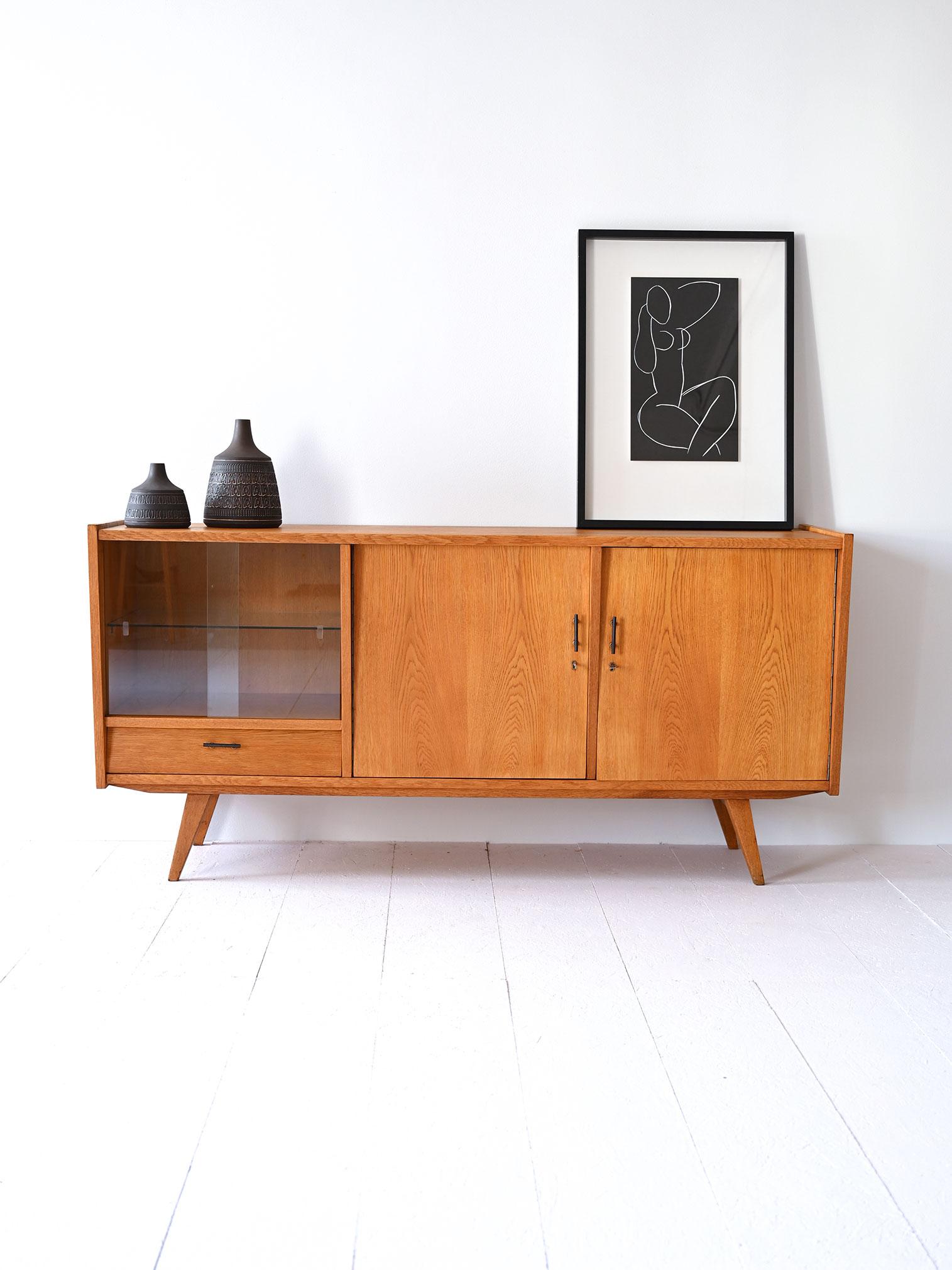 Un sideboard originale e vintage anni '60 in rovere, caratterizzato da due ante a battenti e un vano con antine scorrevoli in vetro, sotto cui si trova un pratico cassetto. Rappresenta un elegante esempio di design del periodo.

Questo sideboard,
