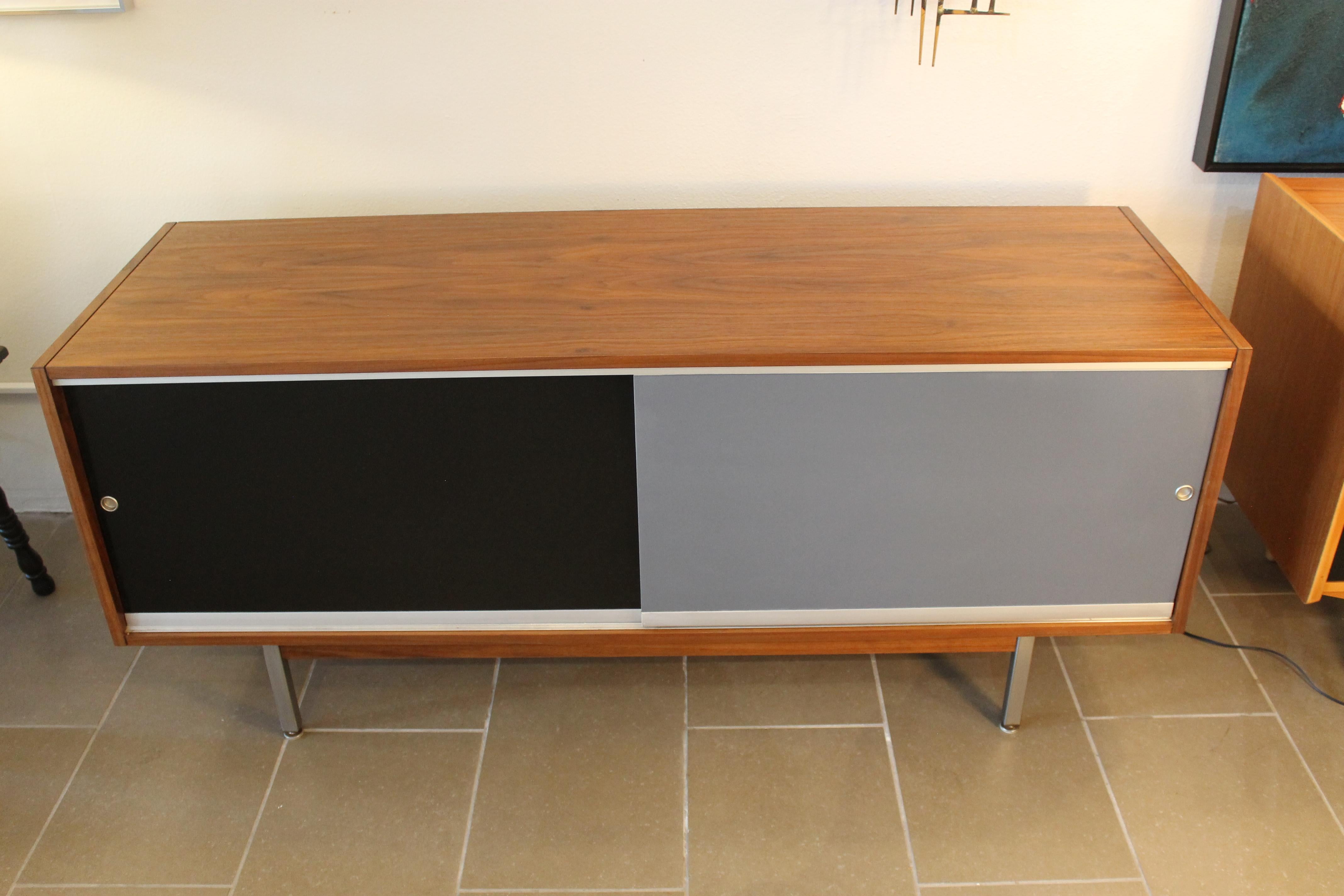 Credenza with black and grey sliders on steel legs. Reminiscent of George Nelson designs.  To the right of cabinet there are 2 drawers and a filing cabinet. The credenza measure 60.25