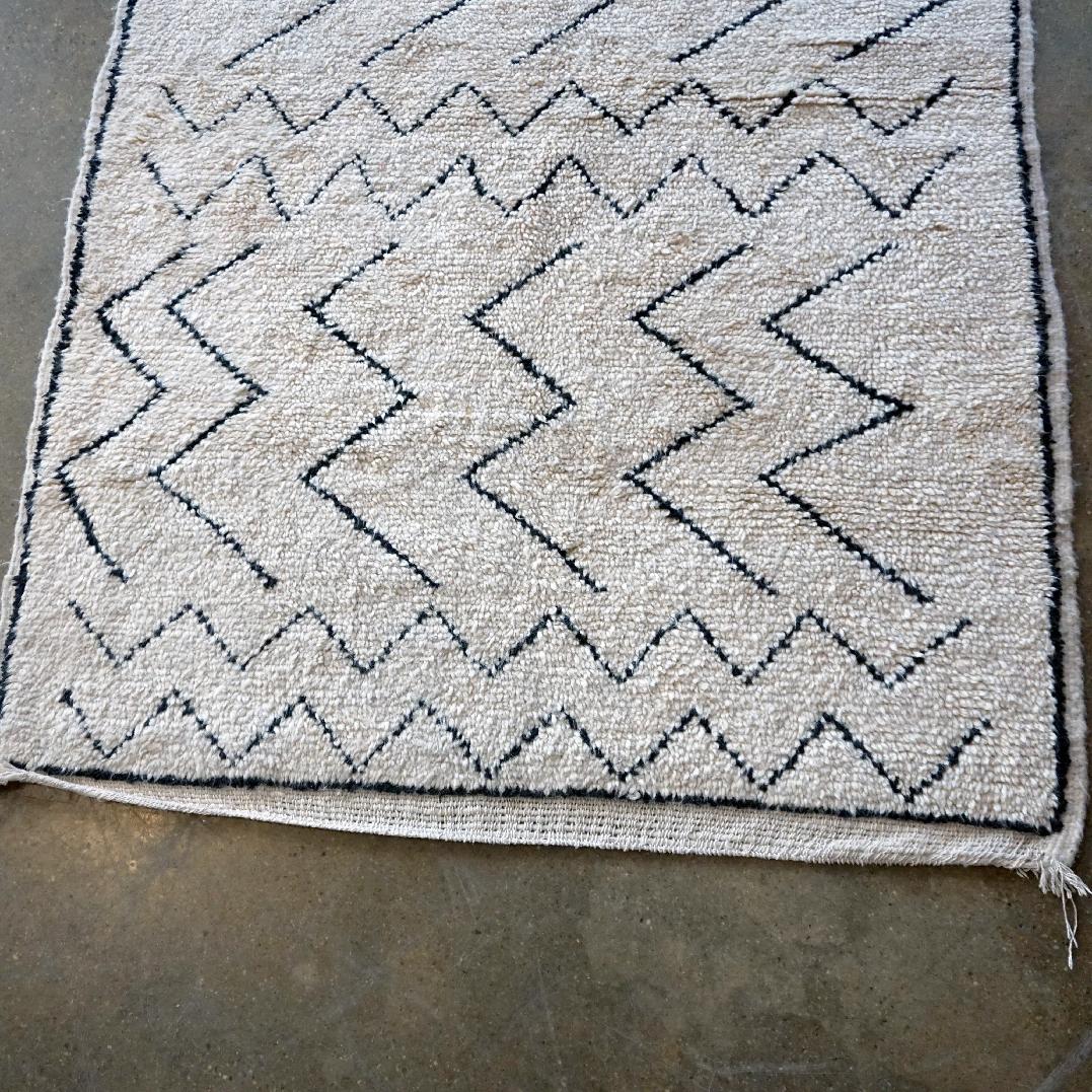 This beautiful and soft  Moroccan Beni Ourain Berber Rug has been hand knotted in the Atlas Mountains and features a  geometrical design and light colors with creme white and black. It is from recent production and in very good condition.
Entirely