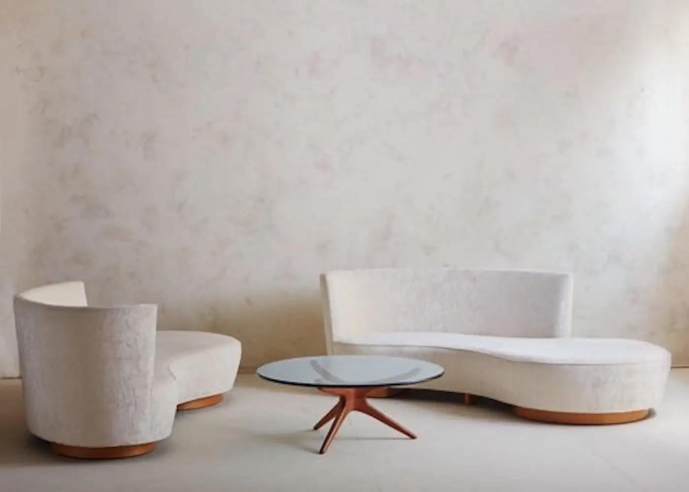 An iconic Crescent sofa designed by Vladamir Kagan in 2005. This sofa has a striking curved profile with a right side facing pouf and a heightened backrest on the left hand side. It stands on two round oak wood plinth bases and has an additional oak