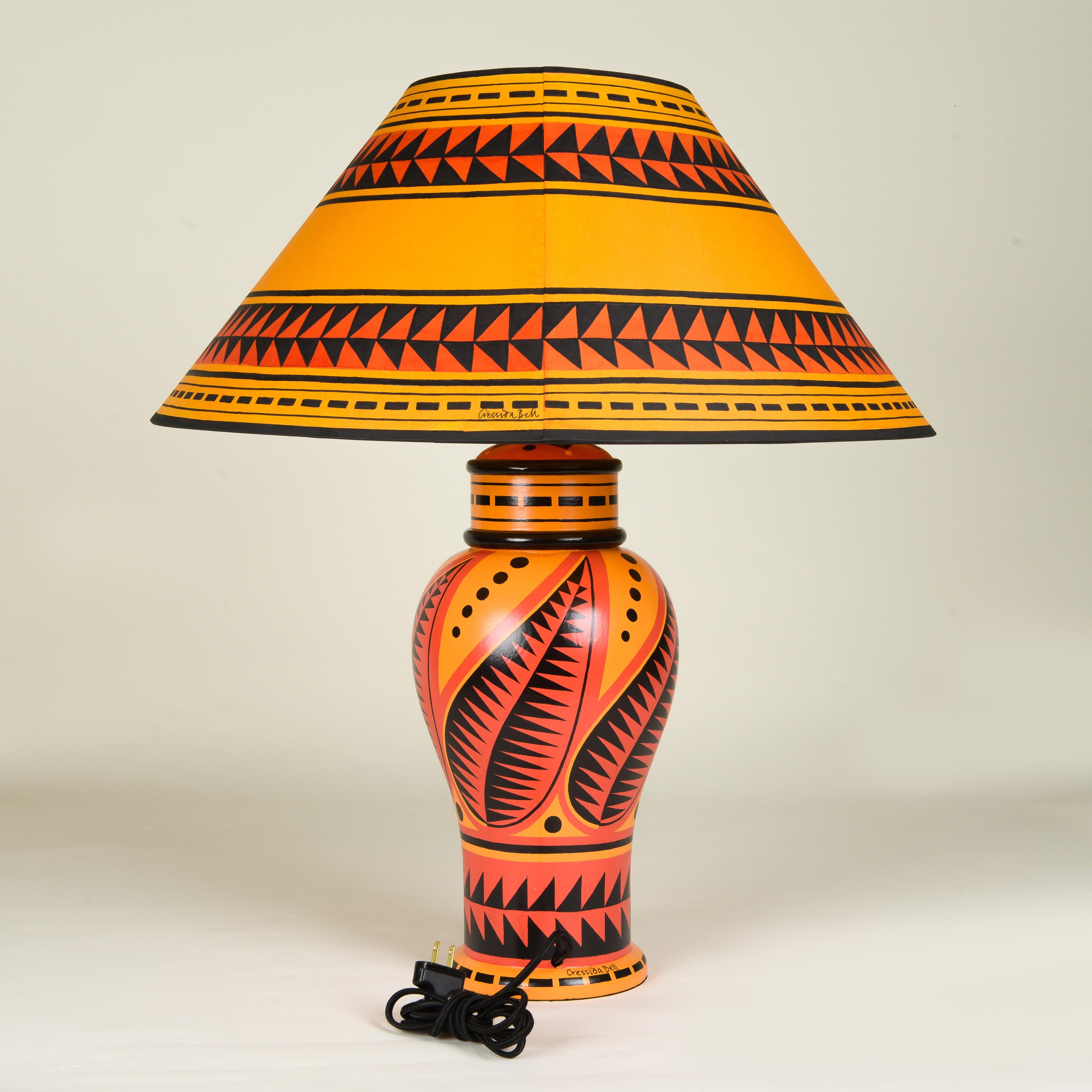 Hand-painted wooden base table lamp with matching shade adorned with red, and black.

Cressida Bell is a British designer specialising in textiles and interiors. From her London studio, she produces a wide range of products including accessories for