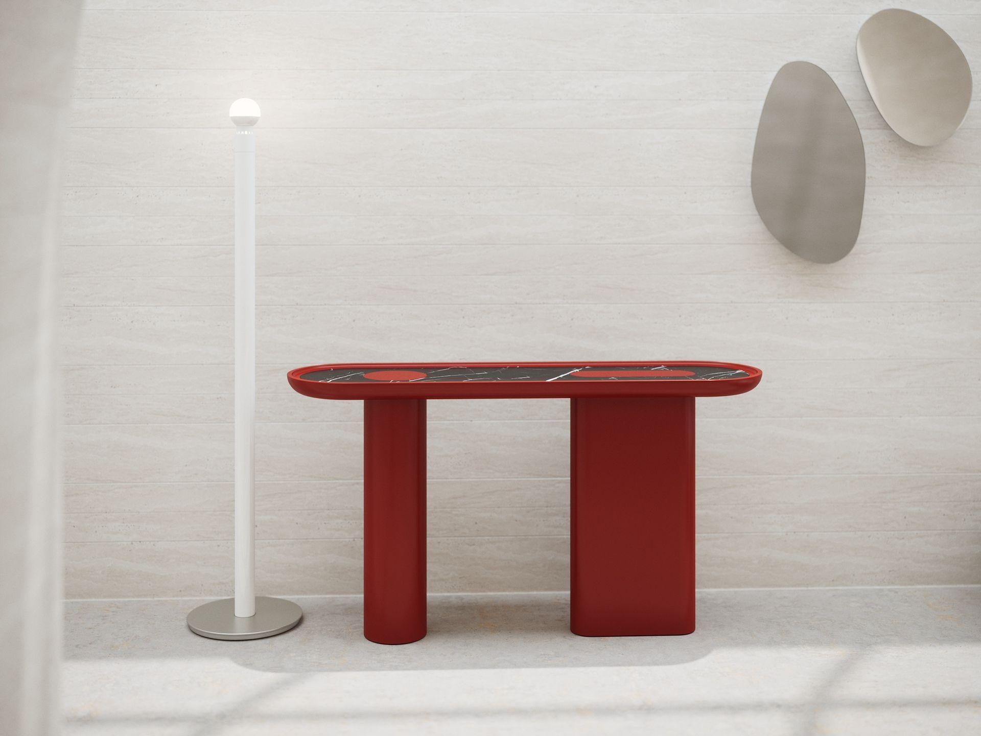 La consolle Creta è completamente laccata in finitura opaca R/Rosso Corallo con una gamba rotonda e una ovale. Il piano sagomato è arricchito da un inserto in marmo nero Marquinia e da dettagli laccati.