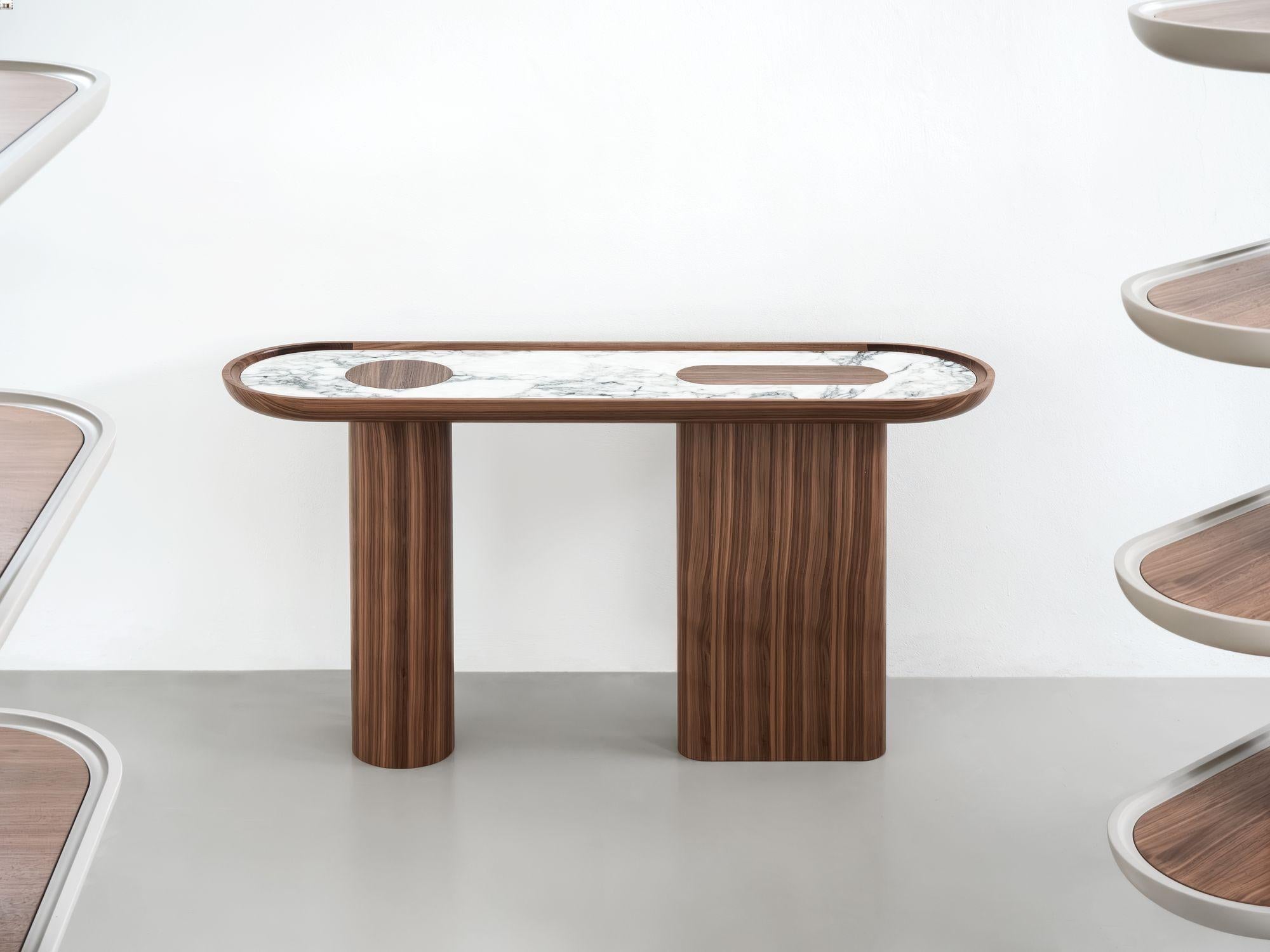 Consolle ovale Creta in Noce Canaletto (Noce Canaletto) con inserto in marmo nel piano sagomato con elementi inseriti in Noce Canaletto.  
Realizzato con marmo Bianco Arabascato.

La forma scultorea e arrotondata e i materiali a contrasto