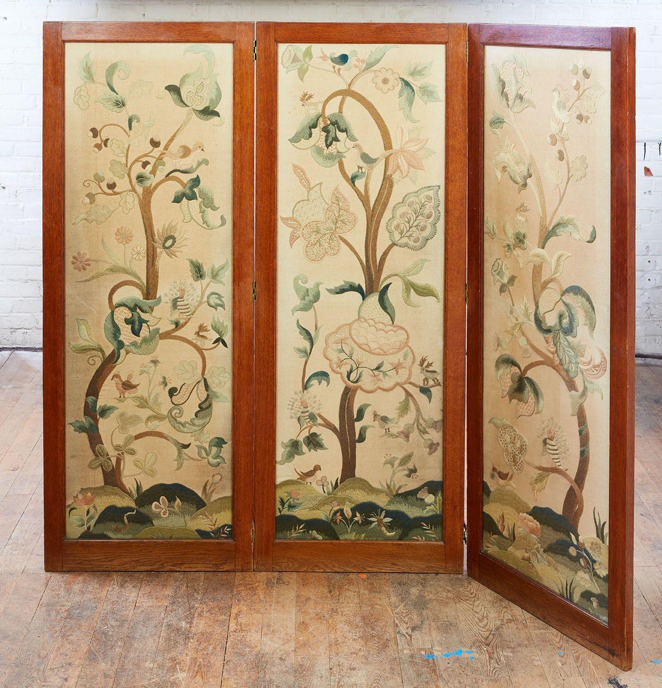 A three paneled English hand-embroidered crewelwork screen in a substantial oak frame with brass hinges. The crewelwork features vine and flower design with birds and deer on a stylized forest surface. Wool stitching on a linen ground. Fine quality.