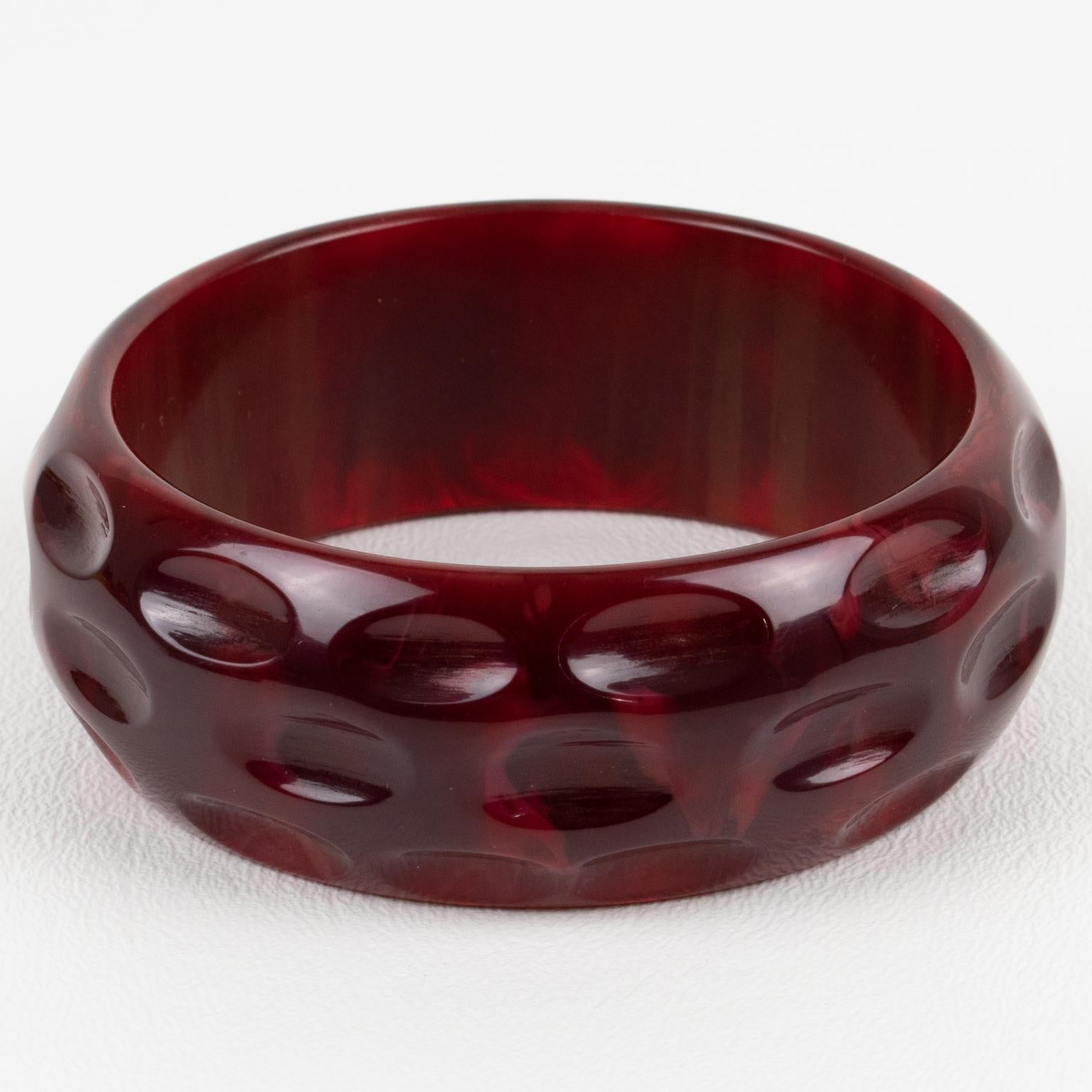 Este impresionante brazalete de baquelita de mármol rojo carmesí tiene una forma abombada con diseños geométricos y profundamente tallados. El raro color es un tono rojo mármol intenso con remolinos turbios. 
Dimensiones: El diámetro interior es de