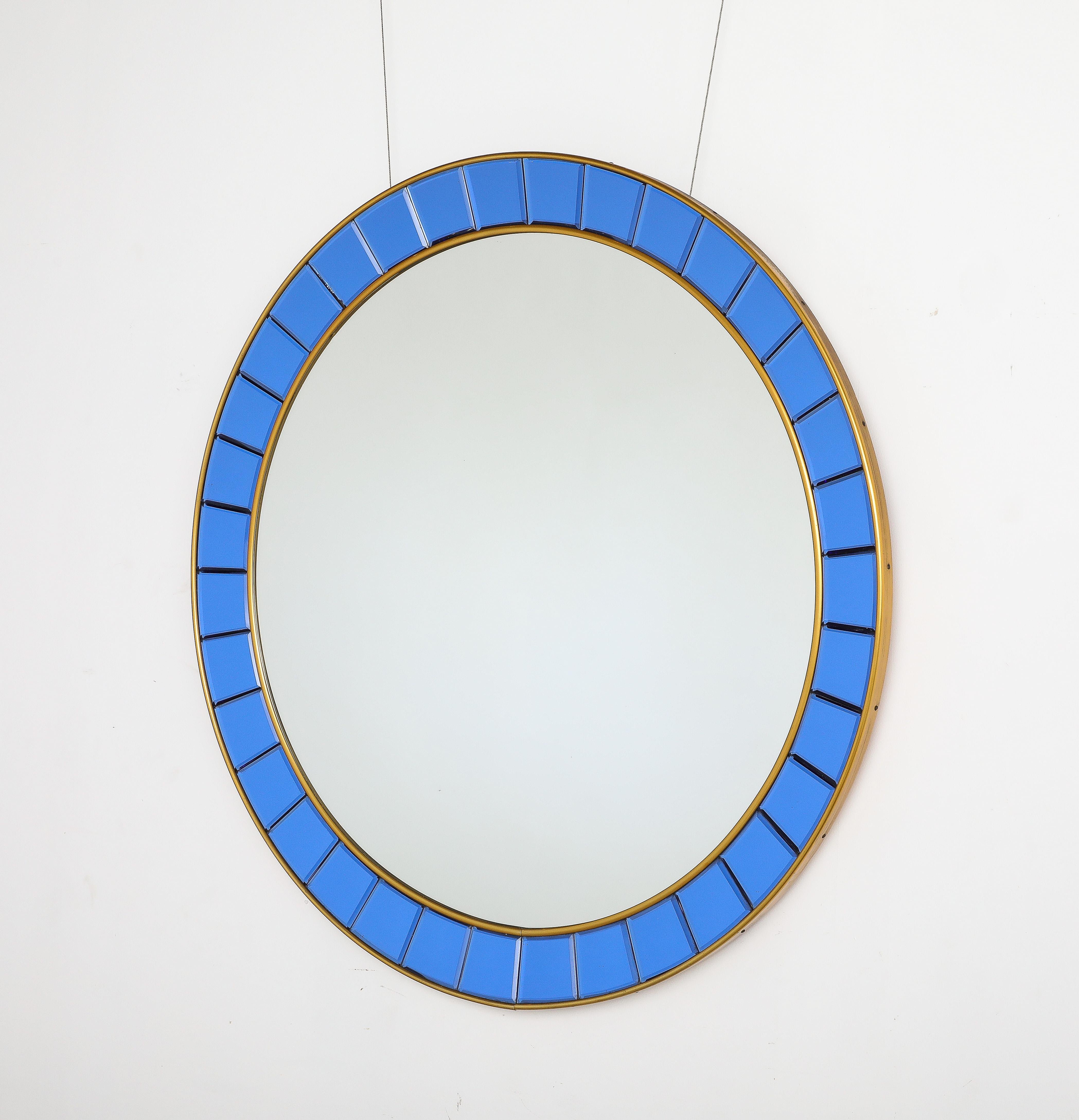 A Cristal Art circular wall mirror, model No. 2679.  

The circular form with hand-crafted beveled or faceted crystal glass pieces framed by gilt-brass borders and outer molding. The faceted glass pieces are realized in a stunning electrifying blue