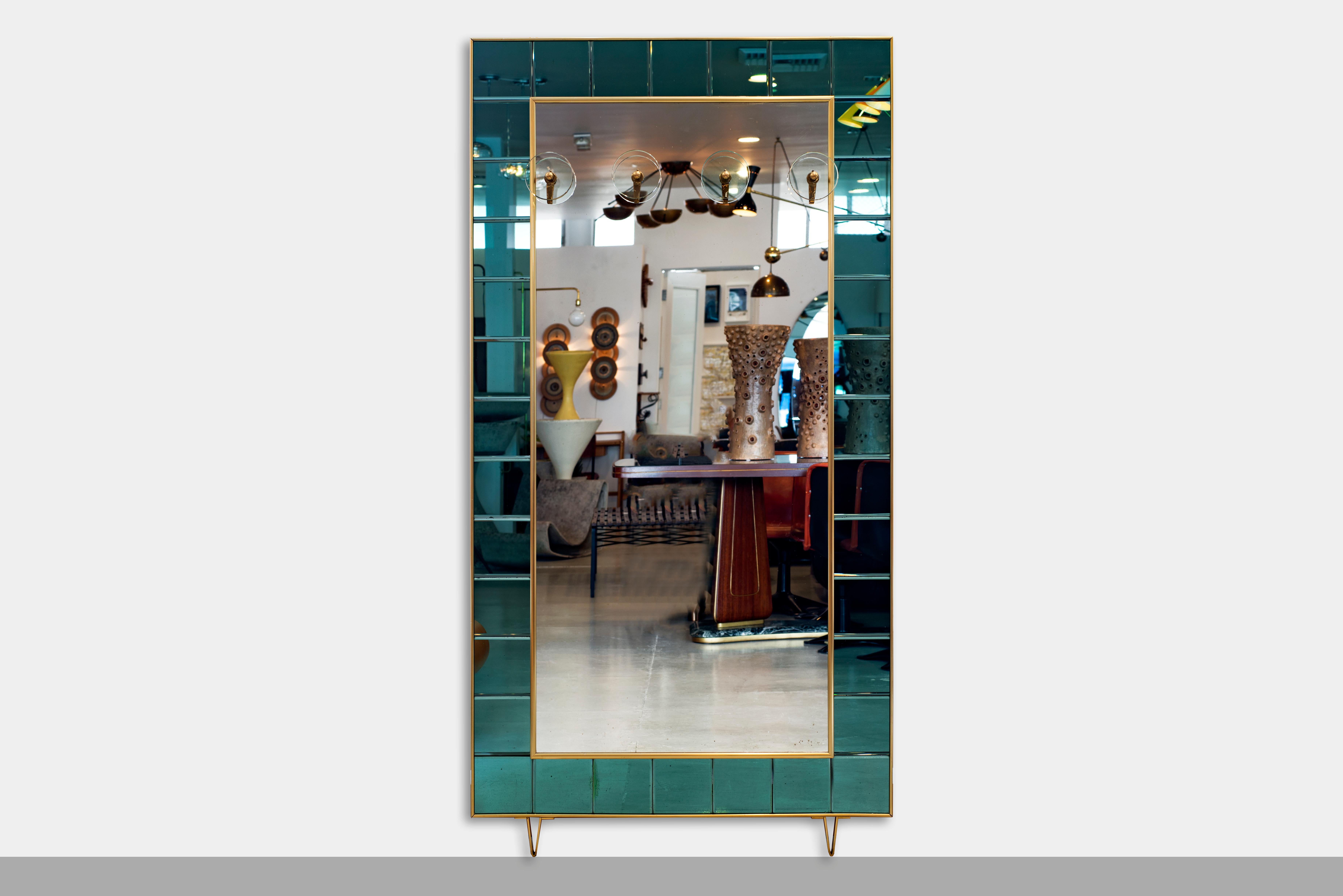 Giant Cristal Art mirror with green-blue glass square tile frame and brass edge detailing. Four glass and brass disc hooks. Mirror floats on two angular brass feet. Stunning piece for an entryway or bedroom.