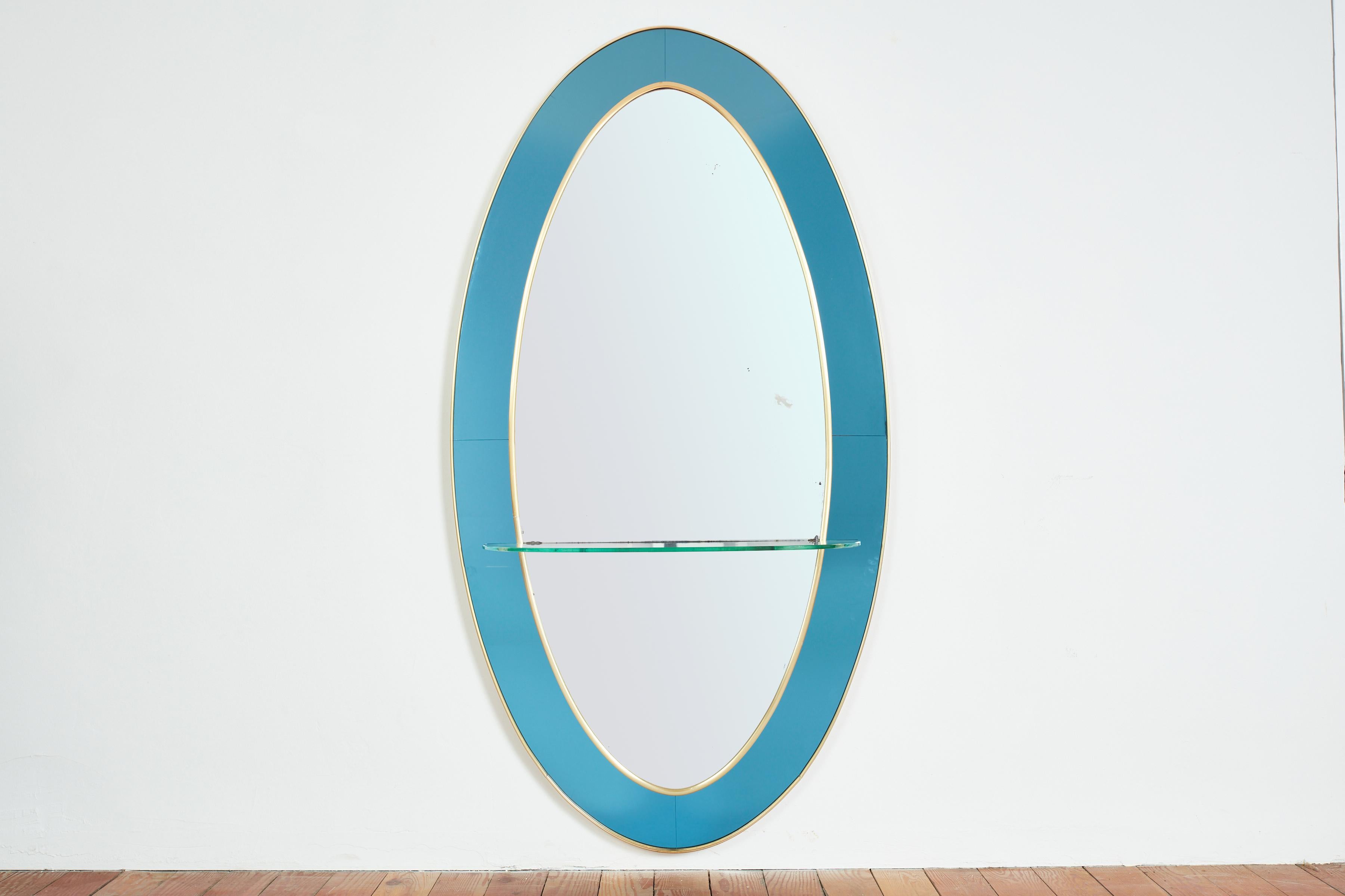 Magnifique grand miroir mural Cristal Art avec étagère en verre bleu brillant et cadre en laiton. 
Forme ovale avec miroir patiné d'origine et verre bleu foncé. 

Italie années 1950