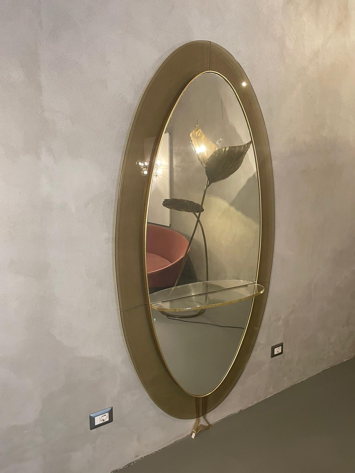 Floor mounted mirror manufactured by Cristal Art in Italy, 1960s.
The mirror is framed with four colored glass panels matching each other that assume an oval shape.
The oval mirror laterally is surrounded by a brass frame and features a glass