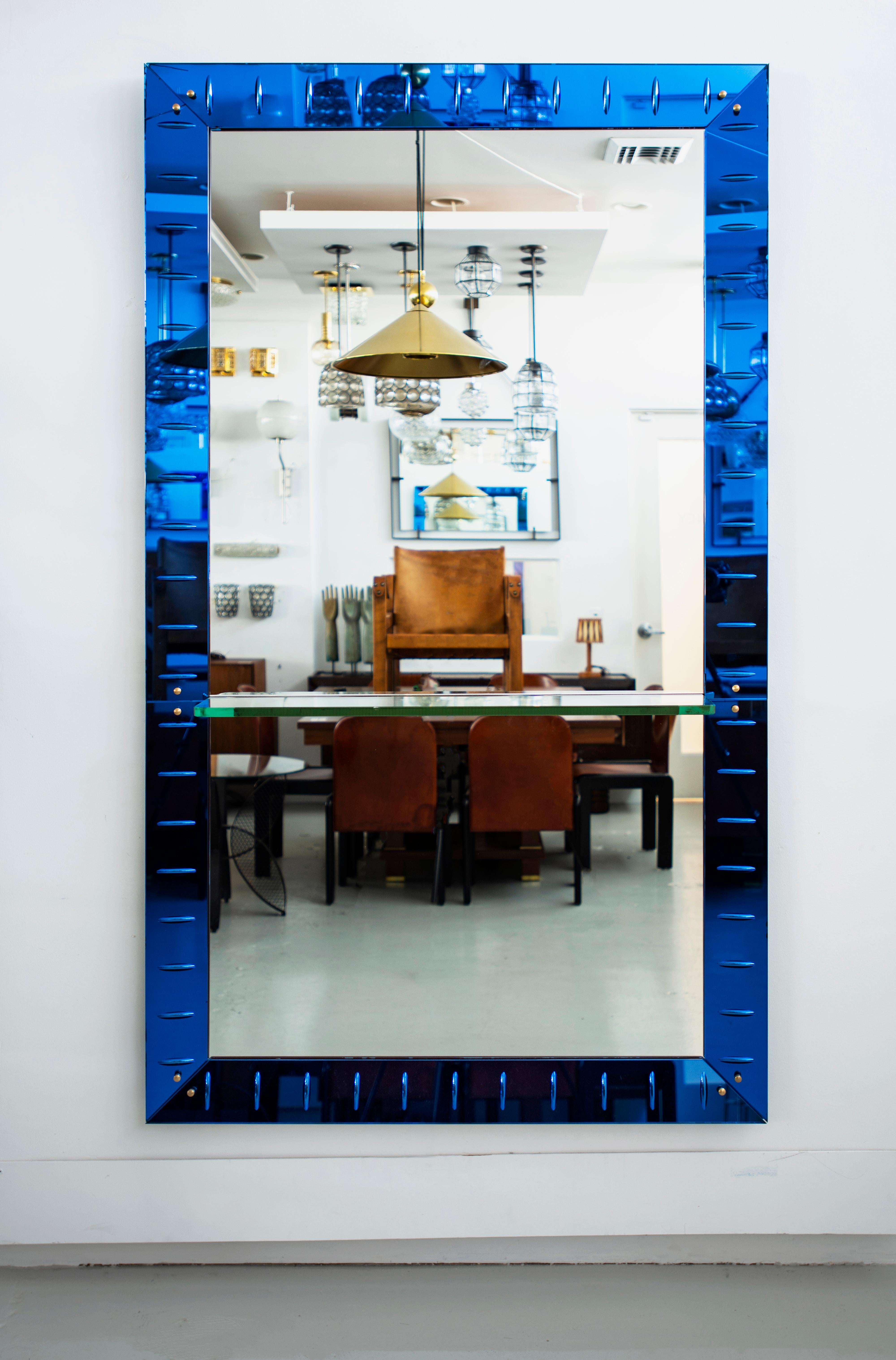 Large floating wall mirror by Cristal Arte. Bright blue colored glass mirror frame and beveled glass shelf. Chip on one corner.