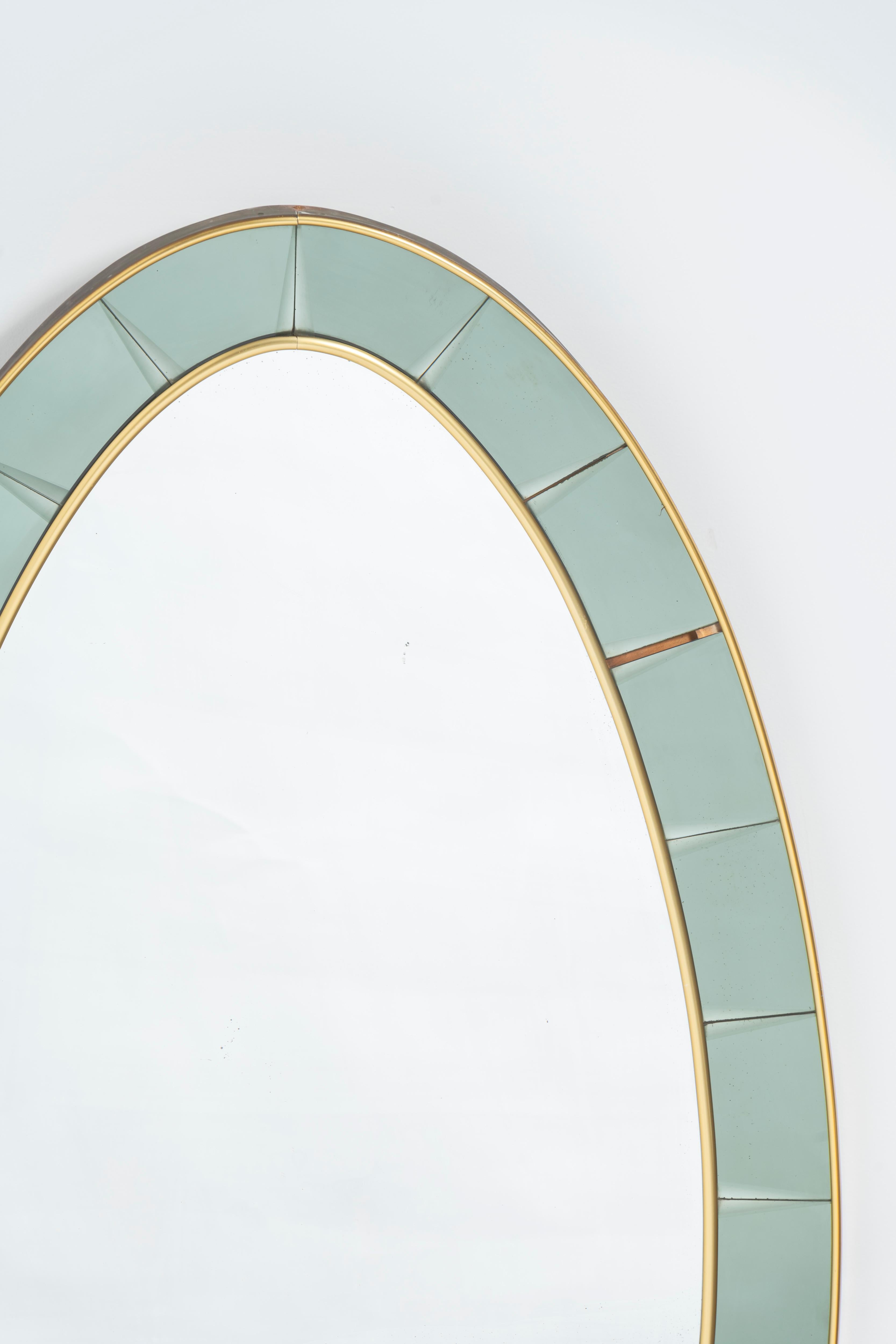 With its strong oval shaped design, this beautiful mirror was made by Cristal Arte in the early 1950s. This wall console mirror features a light green colored crystal edging with brass frame border and trim, with a thick Murano glass shelf. A