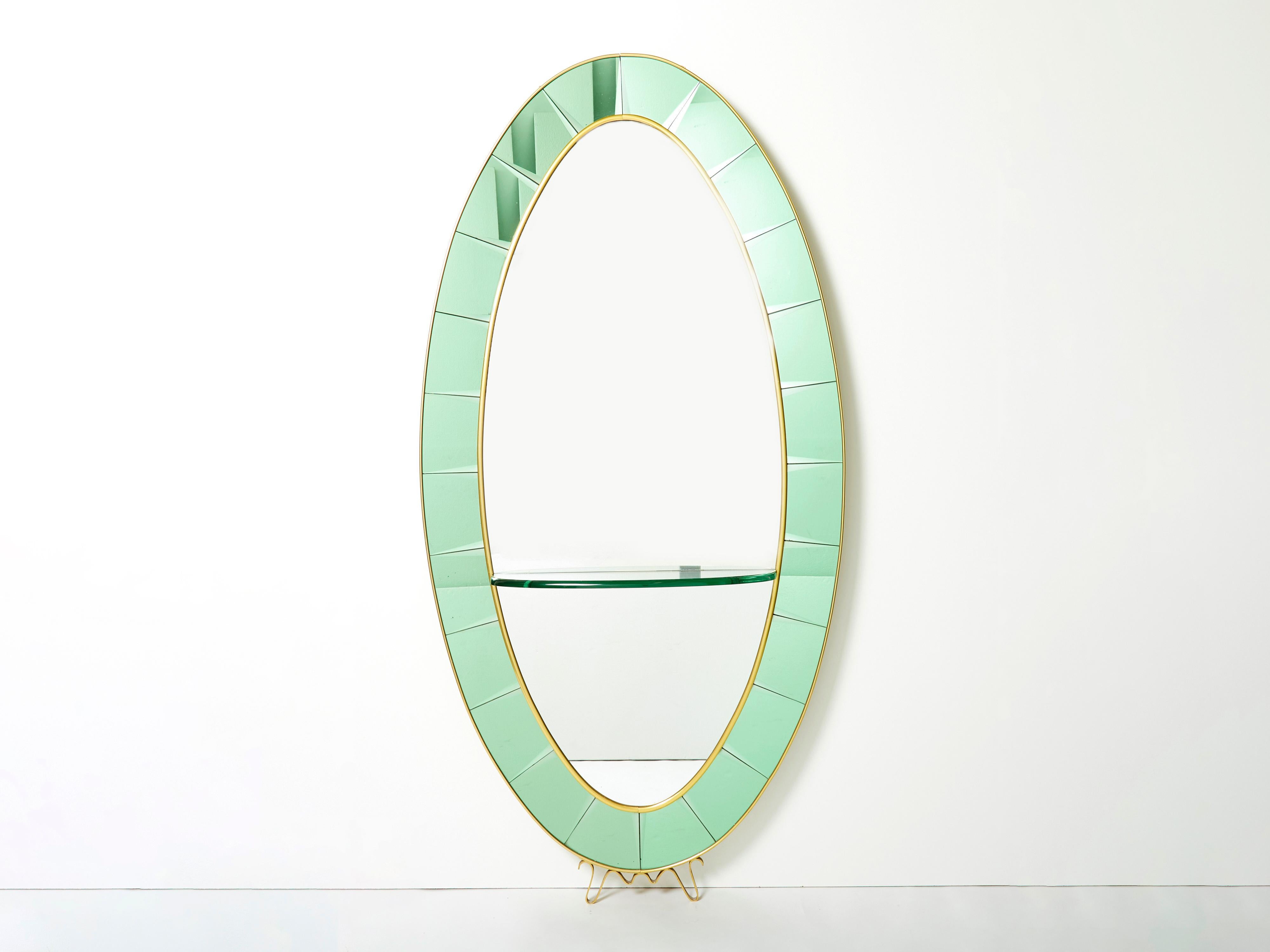 With its strong oval shaped design, this beautiful mirror was made by Cristal Arte in the early 1950s. This wall console mirror features a light green colored crystal edging with brass frame border and trim, with a thick murano glass shelf. A