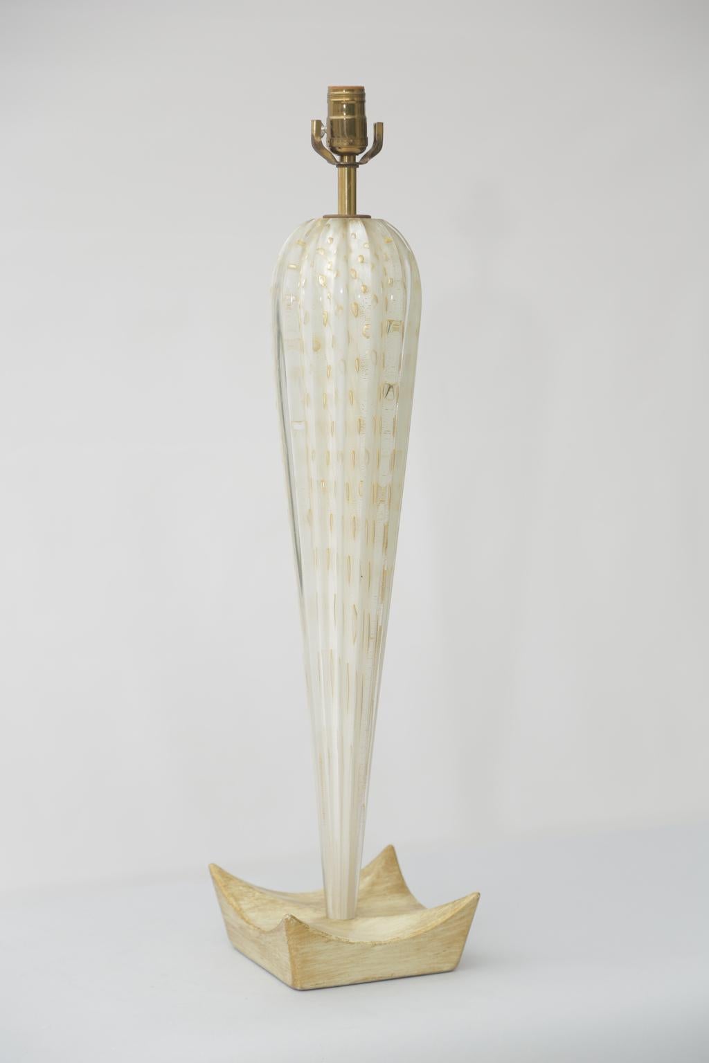 Hand-blown murano glass table lamp, attributed to Barovier e Toso, having a reeded, inverted-teardrop form, gold flecks and bubbles encased in clear glass over opaque white glass, on a concave wooden base. 

Stock ID: D3163.