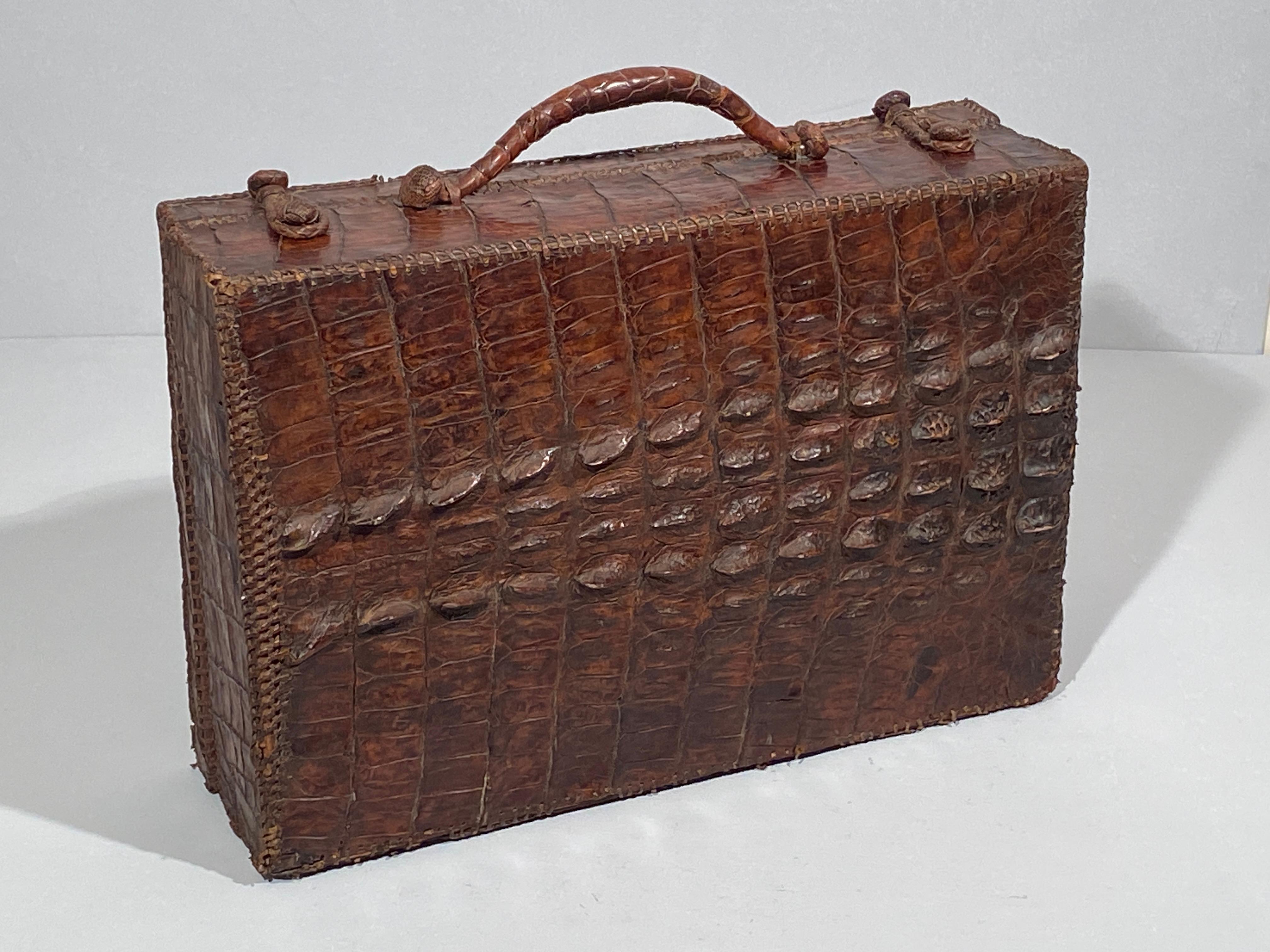 Antique suitcase made of crocodile leather featuring prominent hornback scales hand stitched with fine leather lacing, an attractive antique reptile skin suitcase with a beautiful patina,  suitable as a decoration object or useful storage in your