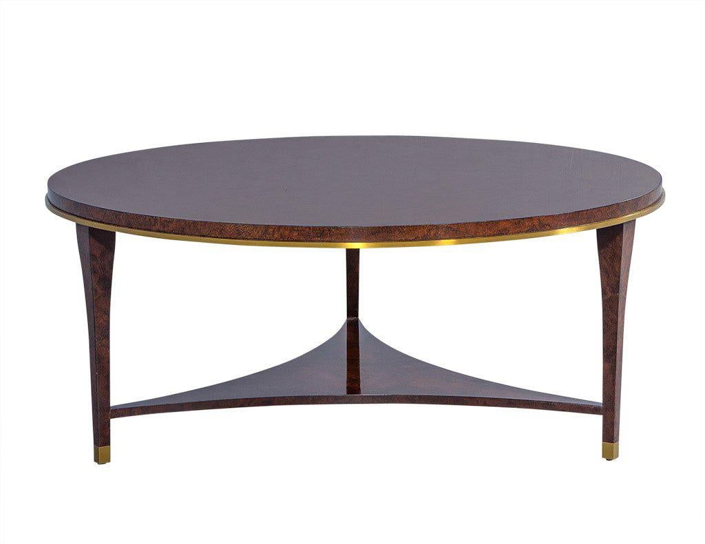 Designed by Aerin, a simple and elegant silhouette defines this gorgeous cocktail table. With a deep and richly finished burl wood round top, trimmed with brushed brass, a lower shelf and asymmetrical appeal this piece presents intrigue and