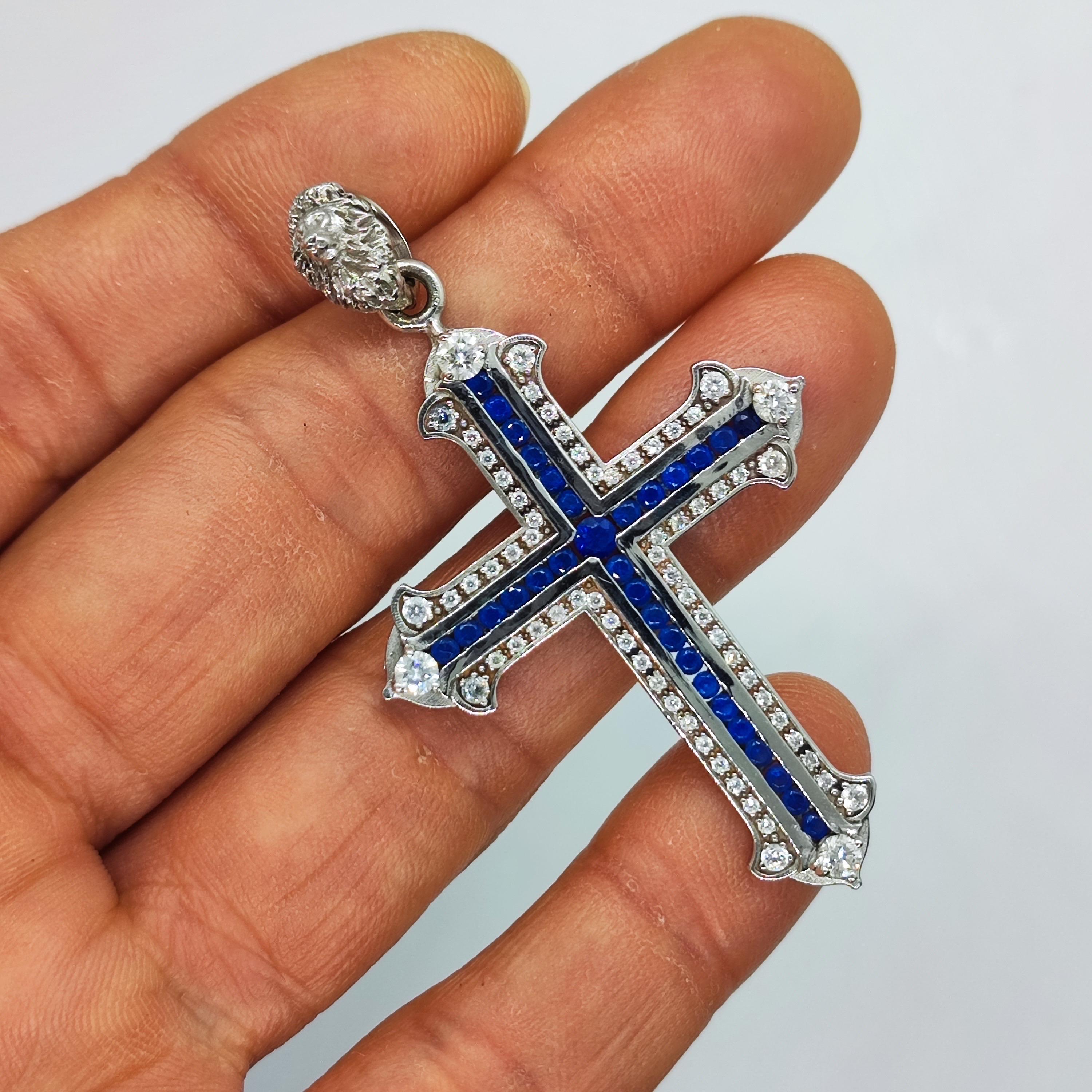 18 kt Weißgold Kreuz 
Mit blauen Saphiren und Diamanten.
Kreuzhöhe 6,5 cm,
Der obere Teil des Kreuzes ist eine Mikroskulptur in Form eines Löwenkopfes.

Der Löwe ist das Bild des Königtums und die Verkörperung des heroischen Anfangs.
Im Buddhismus