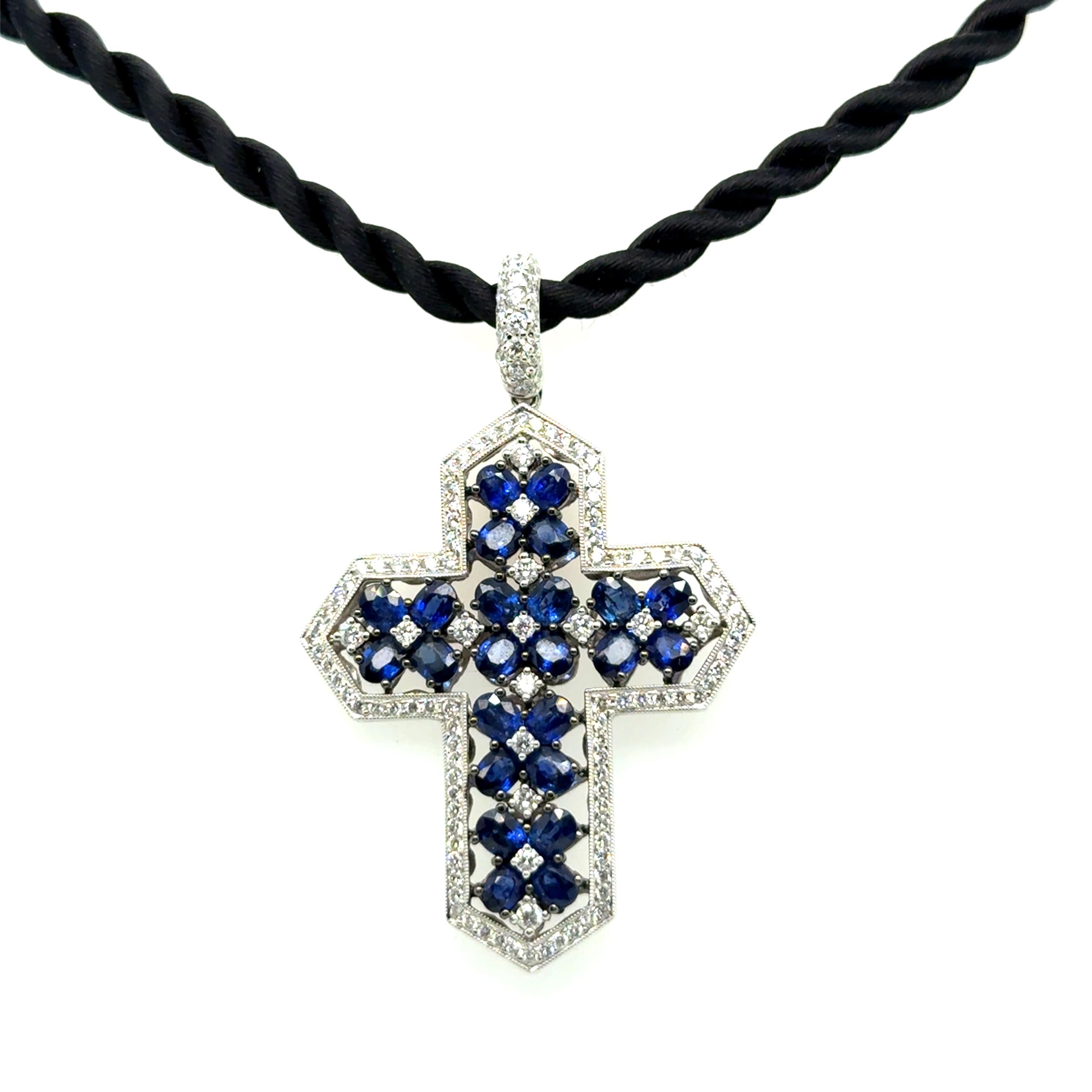 Faites l'expérience d'un luxe raffiné avec ce collier exquis, doté d'un superbe pendentif en forme de croix réalisé en or blanc 18 carats. Orné de 24 saphirs de taille ovale totalisant 5,37 carats et de 131 diamants de taille brillant, de couleur