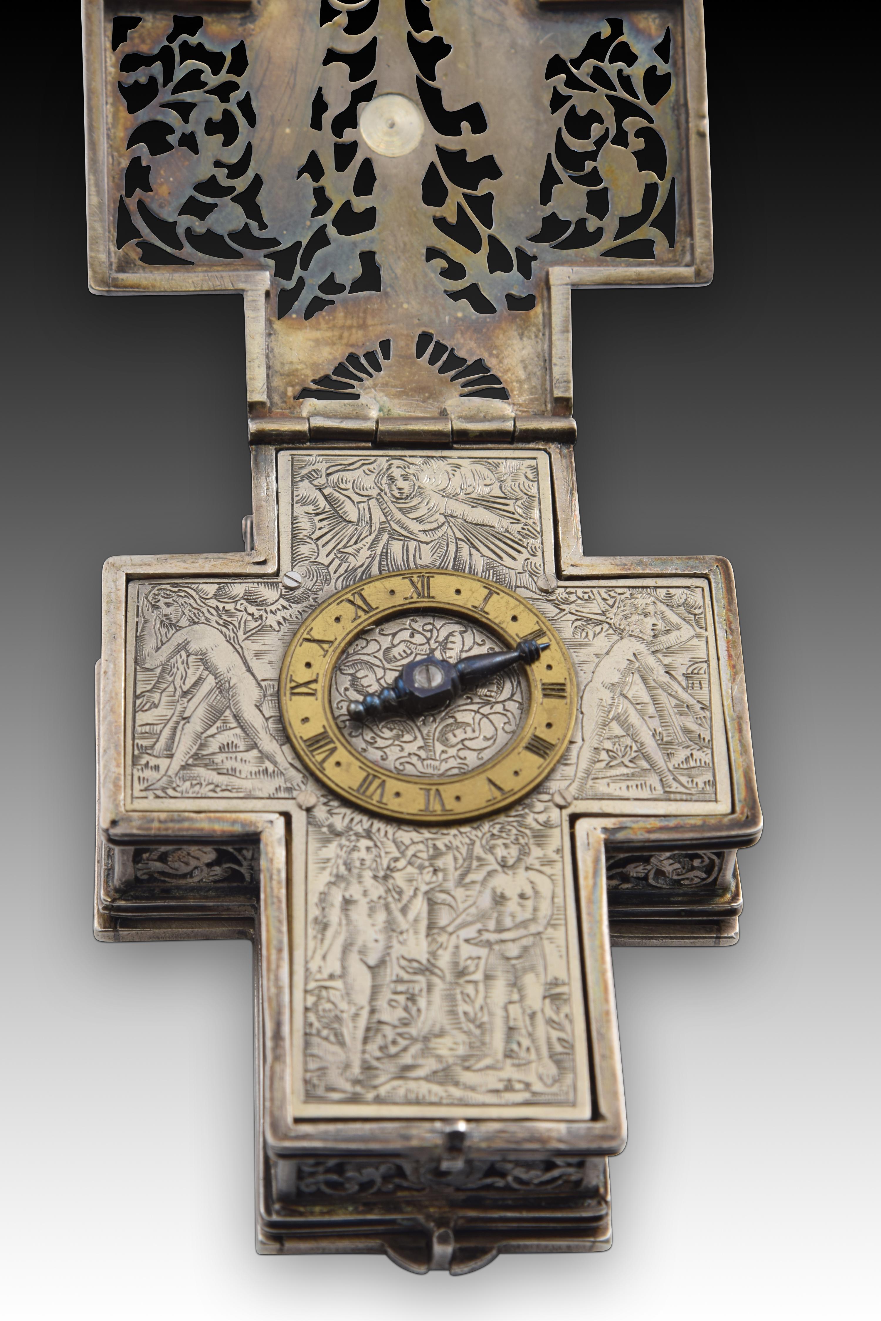 Cross-shaped chest clock. Silver. 17th century. It presents restorations. 
Portable clock in the shape of a cross with an openwork exterior showing Christian figurative scenes and the movement inside, a dial with a golden band with Roman numerals