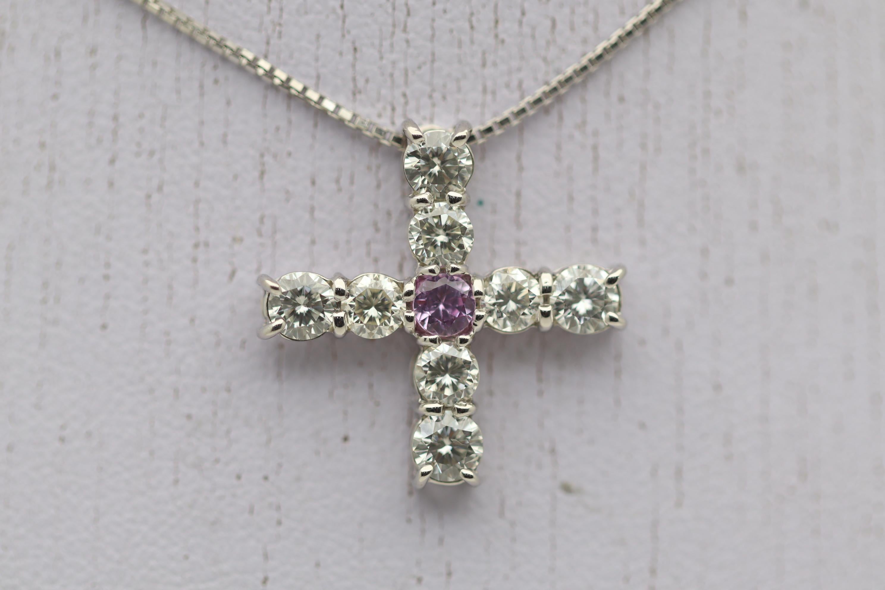 A cross designed pendant featuring 8 large diamonds and a single pink sapphire in its center. The diamonds weigh a total of 1.53 carats and are bright white and clean. In the center of the cross is a 0.20 carat round sapphire with a bright and