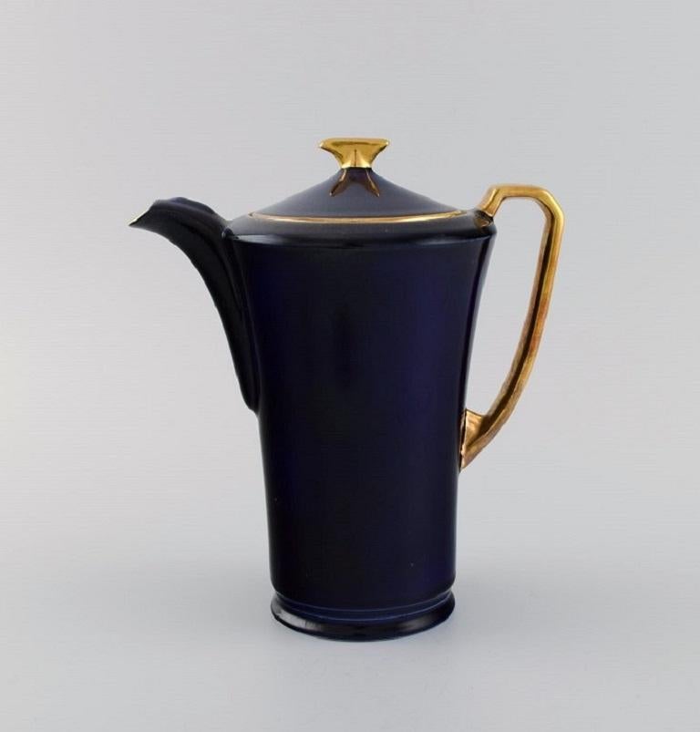 Crown Devon, Angleterre. Service à café Art Déco pour cinq personnes en porcelaine bleu marine, intérieur doré. 1930s.
Comprend cinq tasses à café avec soucoupes, une cafetière et un crémier.
La tasse mesure : 6.7 x 6 cm.
Diamètre de la soucoupe