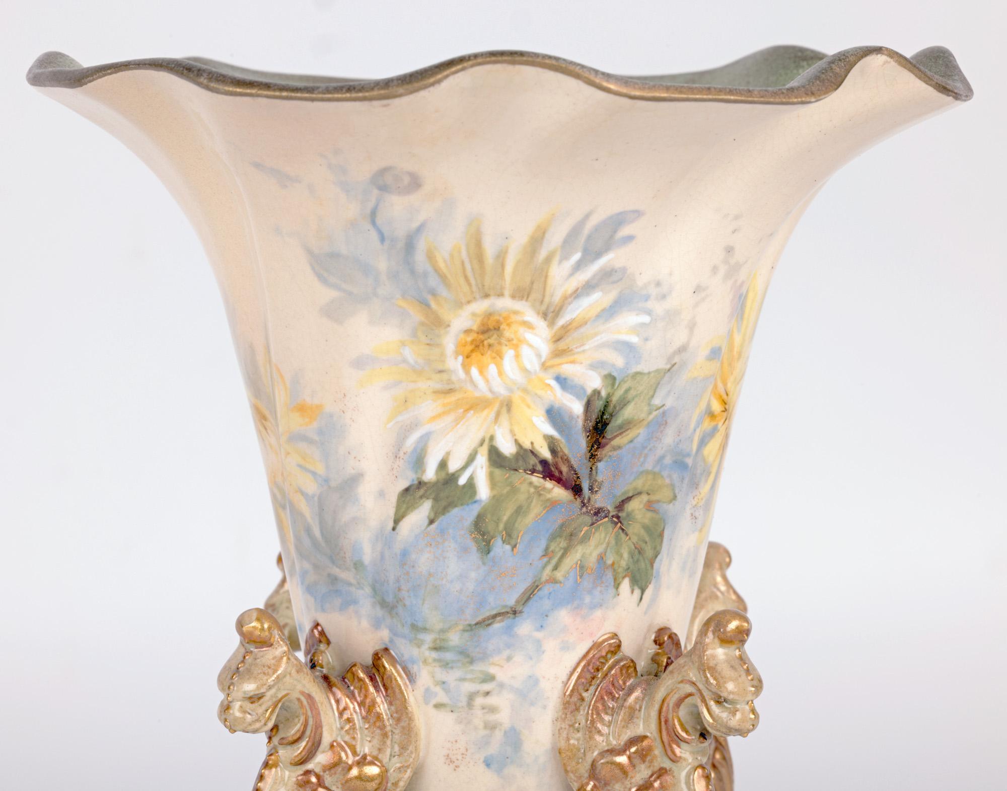 Un vase inhabituel en forme de trompette en Lambeth Ware, peint de motifs floraux et monté avec des créatures mythiques ressemblant à des griffons, datant d'environ 1895. Le vase en grès est surélevé et repose sur une haute base en volutes percées,