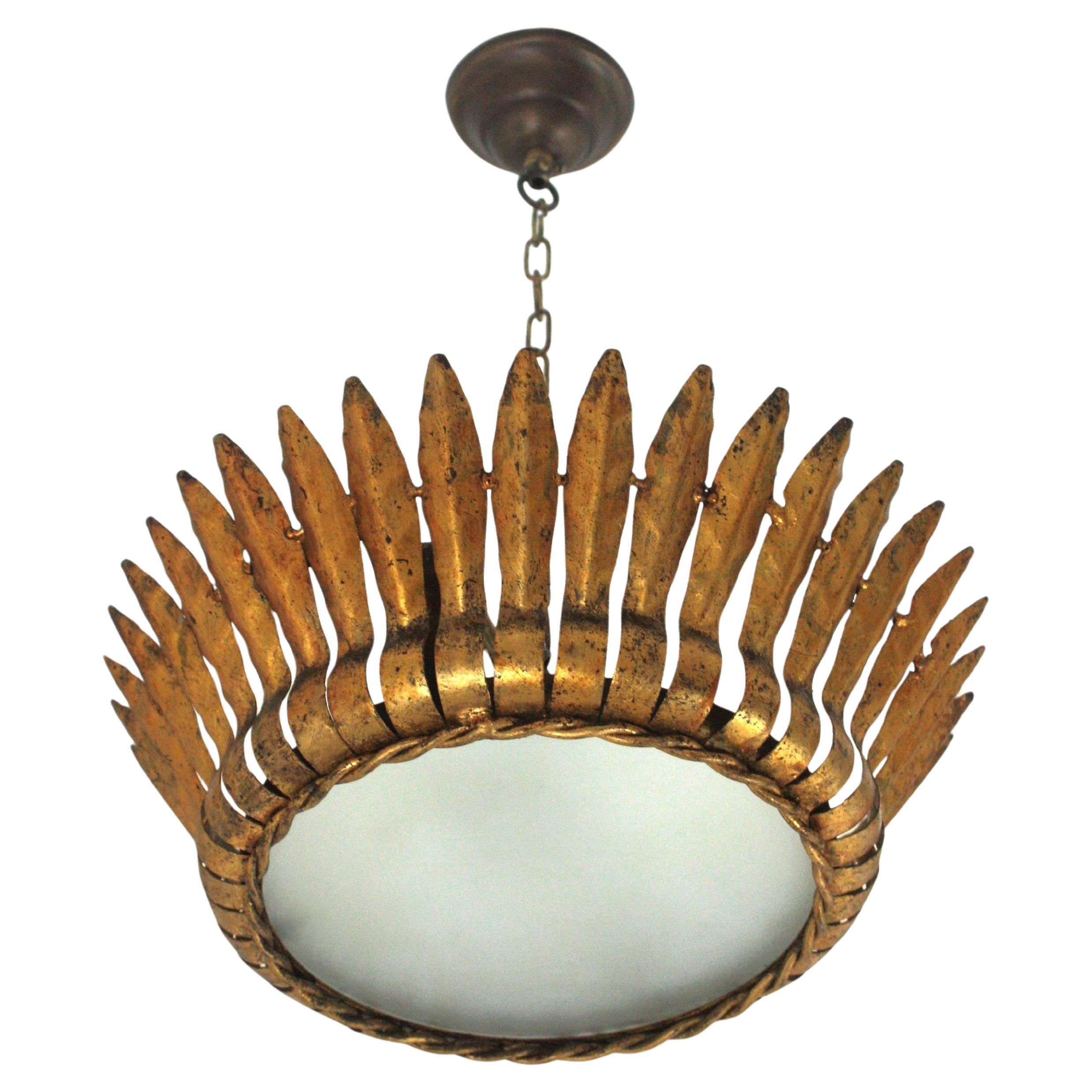 Mid-Century Modern gilt iron crown sunburst flush mount or pendant with leaf motifs surrounding a central frosted glass diffuser, Spain, 1950s.
Handcrafted in hammered iron with gold leaf finishing.
It has a twisted iron rope surrounding the glass