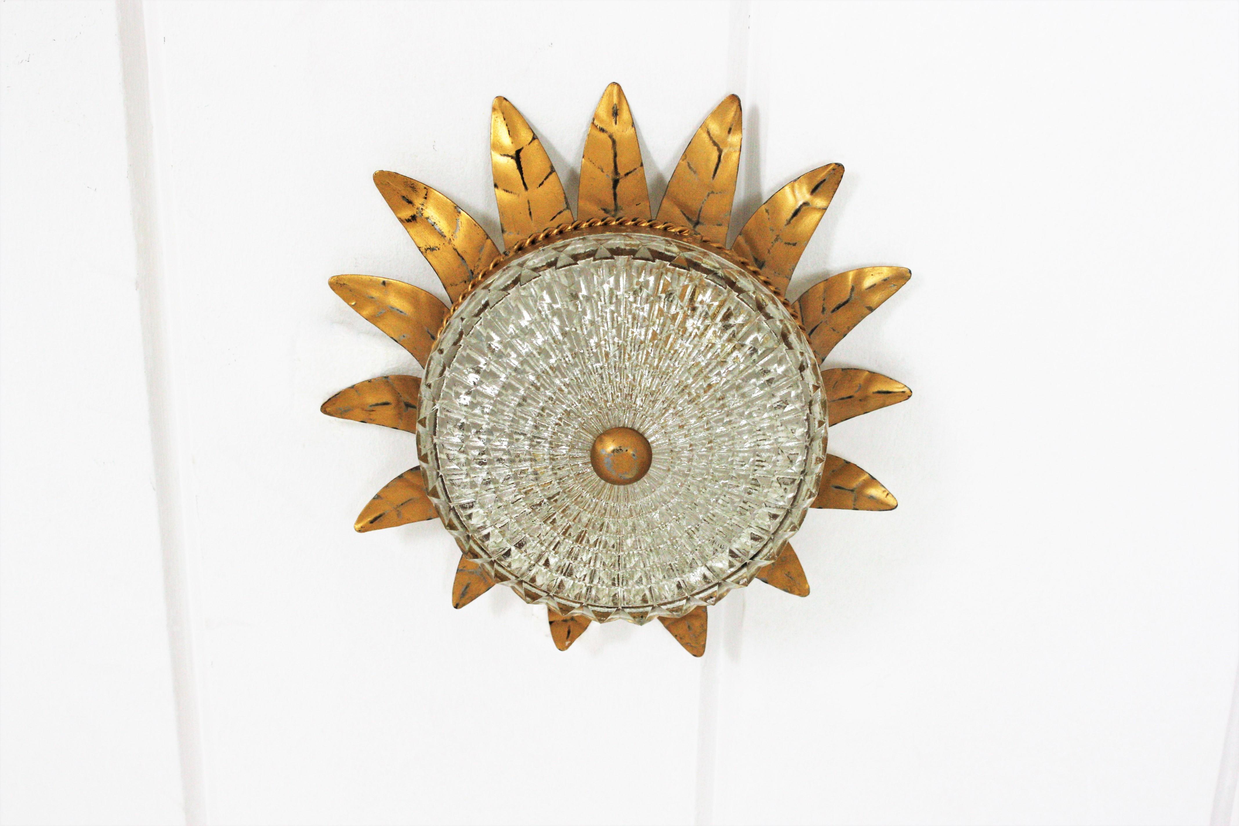 Elegant neoclassical style sunburst crown flush mount from the Mid-Century Modern period, Spain, 1950s.
This ceiling fixture features a gilt iron sunburst crown shaped structure with a pressed glass shade with a gilt iron finial.
It has a highly