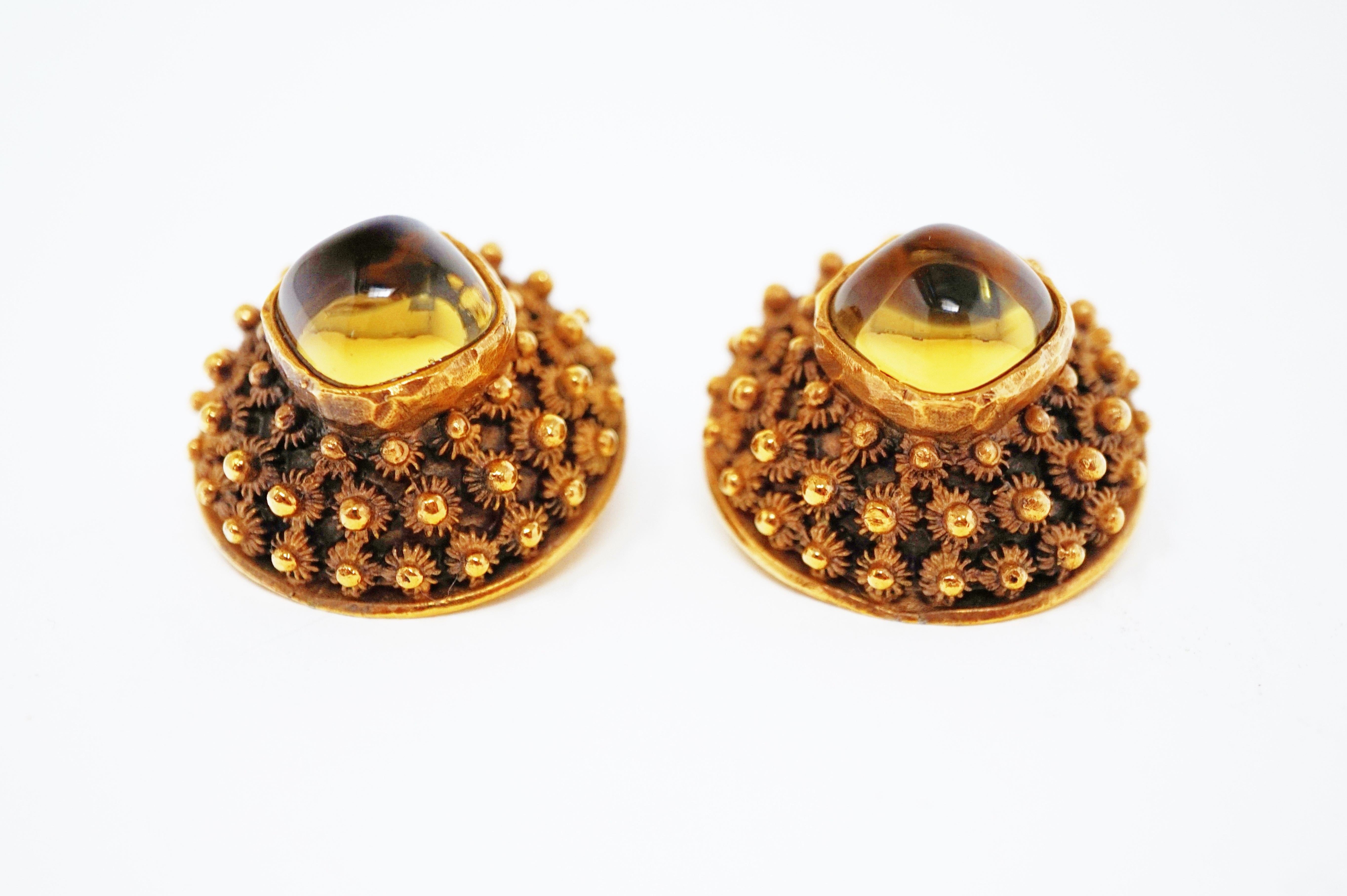 These stylish Brutalist-style clip-on statement earrings by Trifari (circa 1960) are a must-have for costume jewelry collectors.  Truly a statement piece, these earrings are domed and gilded with an antiqued finish. Two Amber-colored glass cabochons