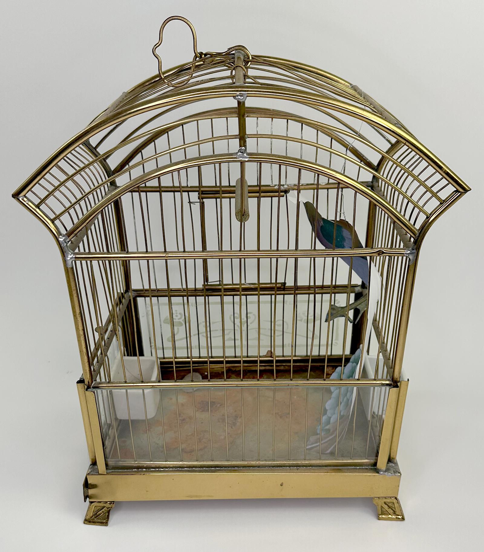 Ein elegant gearbeiteter und charmanter Vintage-Vogelkäfig mit Krone. Hauptsächlich aus Messing gefertigt. Um den Boden des Käfigs herum stehen kleine Glasstücke mit mattierten, geätzten Motiven. 

Dieser Käfig hat Beine, um ihn zu stützen, oder er