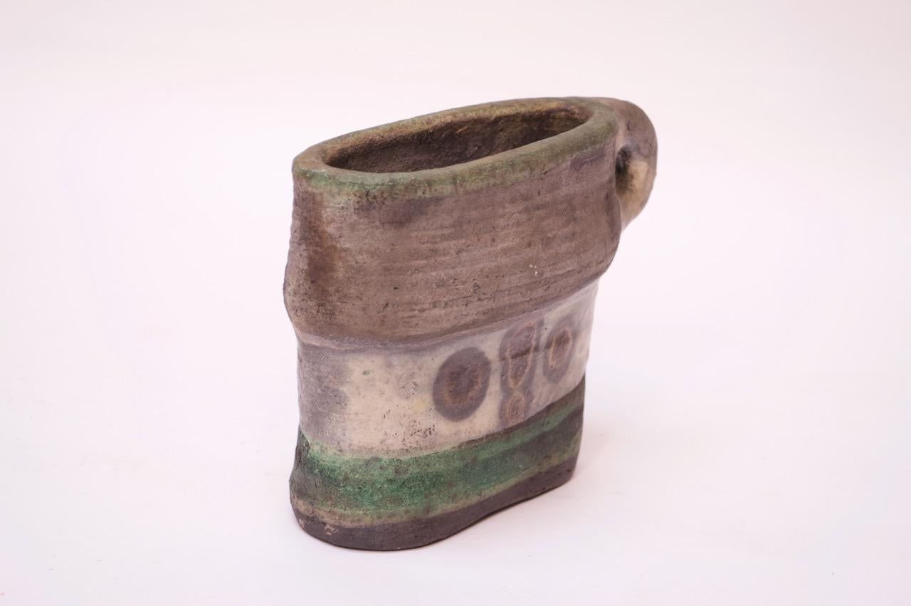 1978 Pollack handled-vase featuring a gray surface with black, green and yellow decoration. Crude by design enhanced by the unglazed finish. 
Incised 